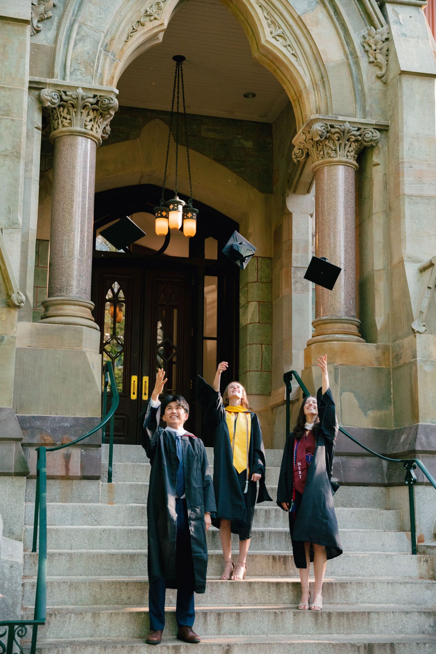 Graduates in caps and gowns gather on ornate stone steps of a university building.