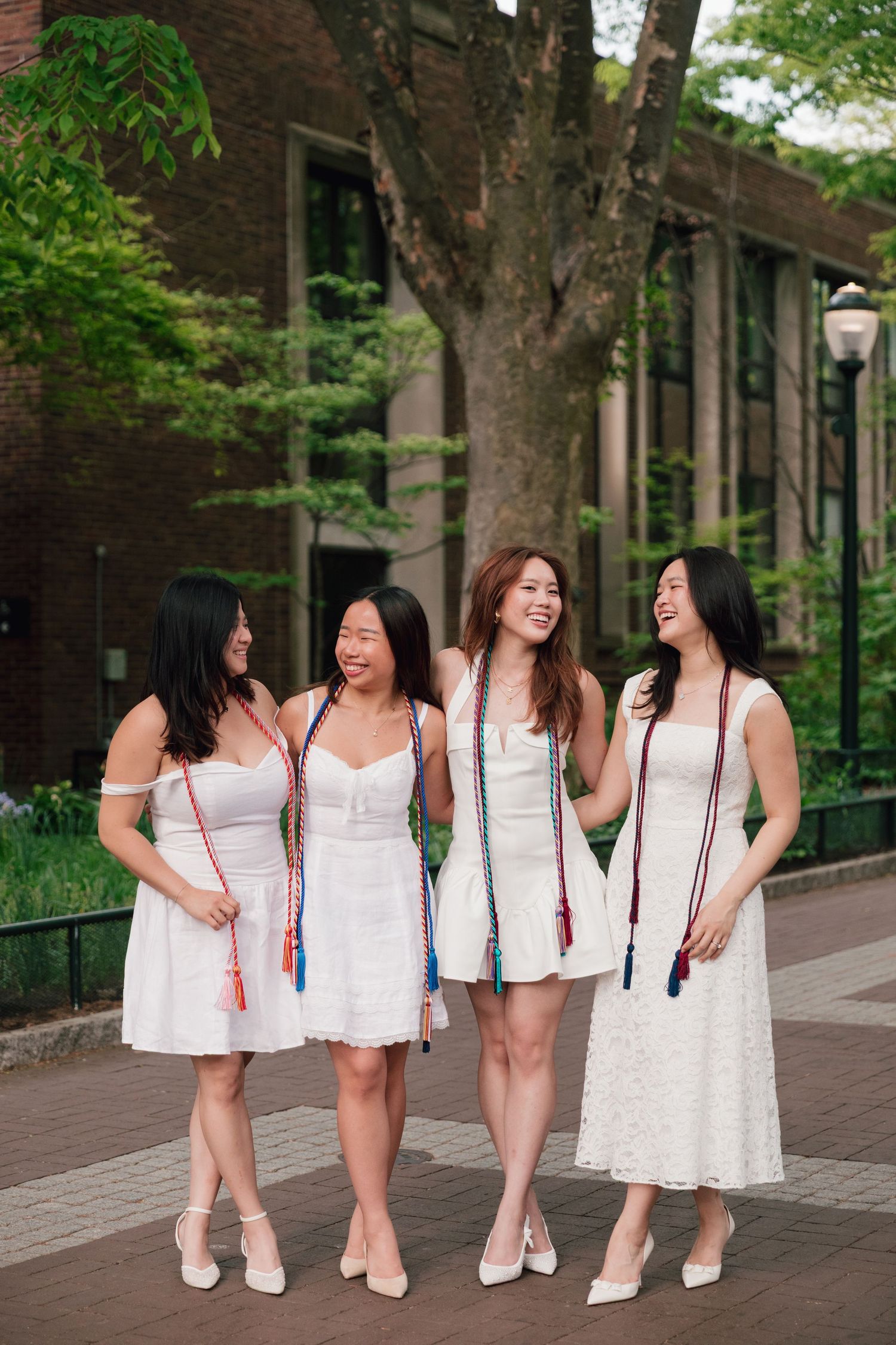 Group photo of graduates in matching white dresses posing together on brick path.