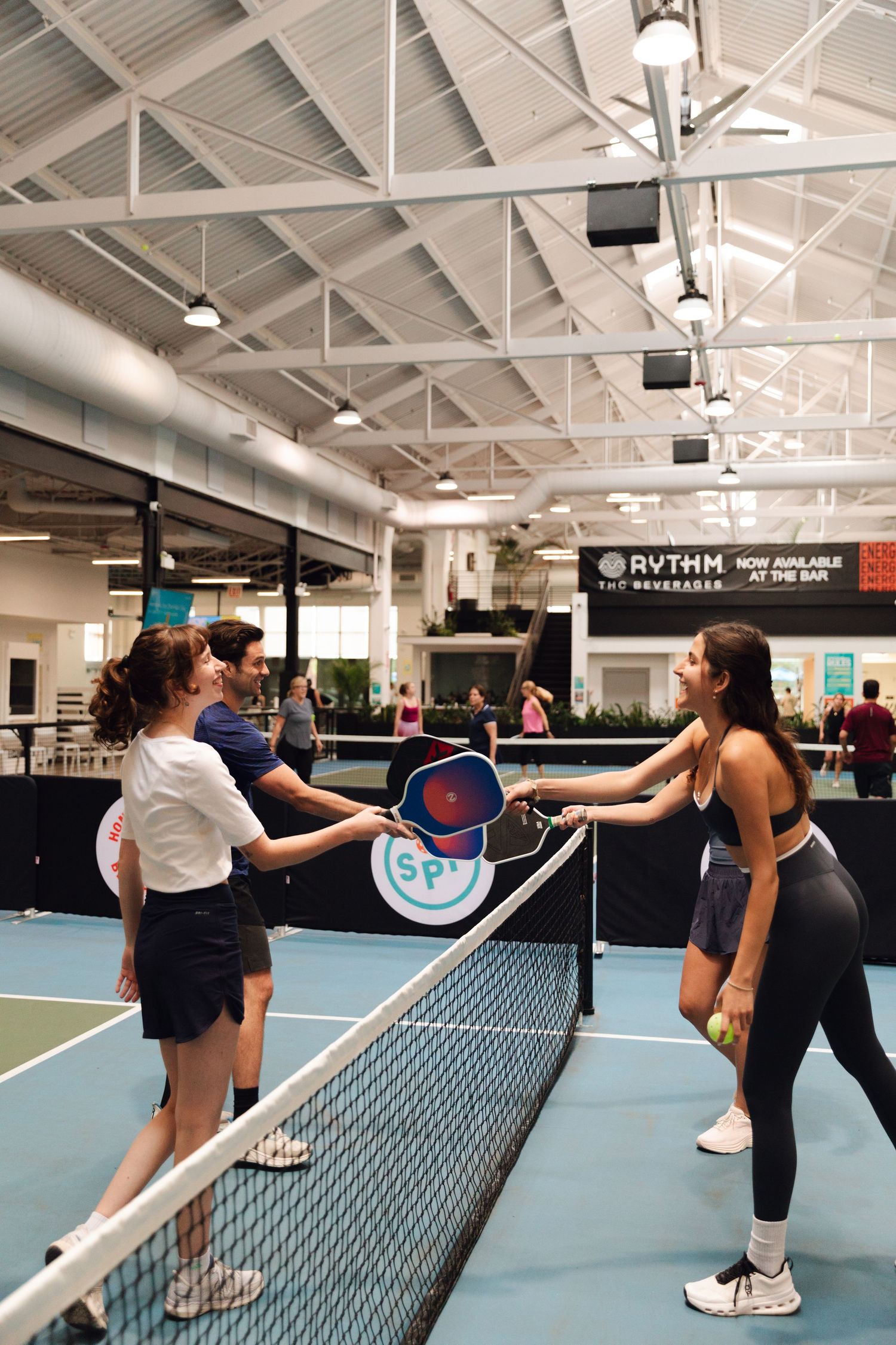 Players shake hands over the net on an indoor pickleball court at a modern sports facility.