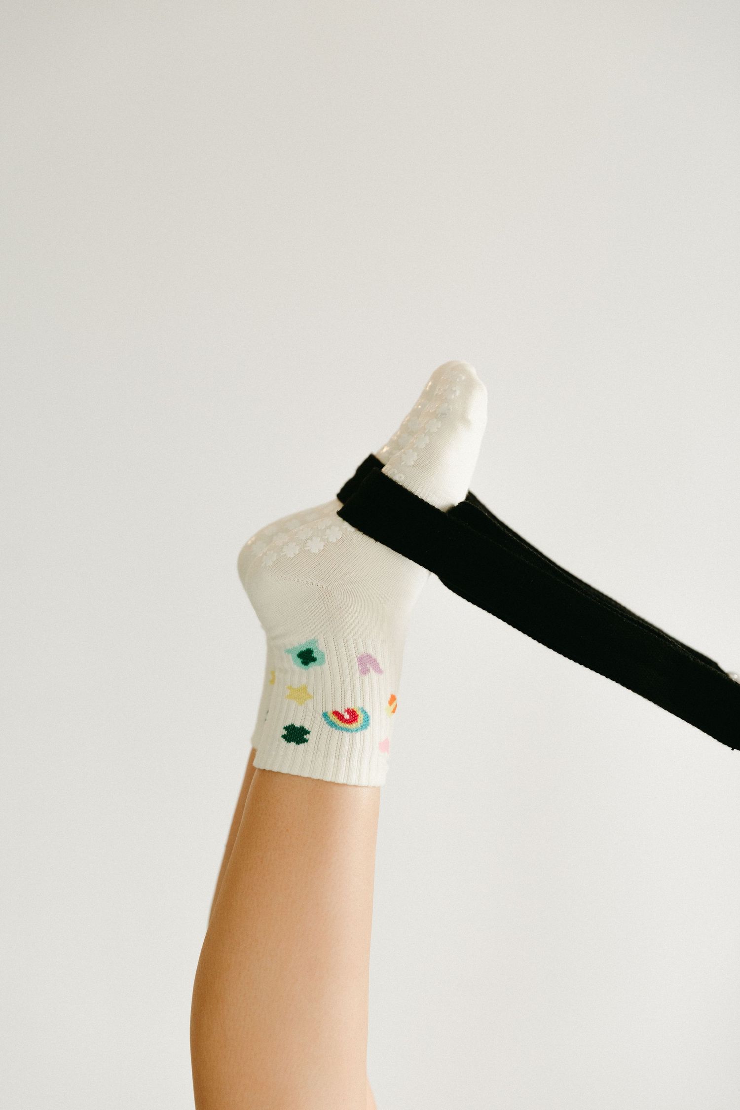 White ankle socks with colorful floral embroidery designs paired with black knee-high socks on raised legs.