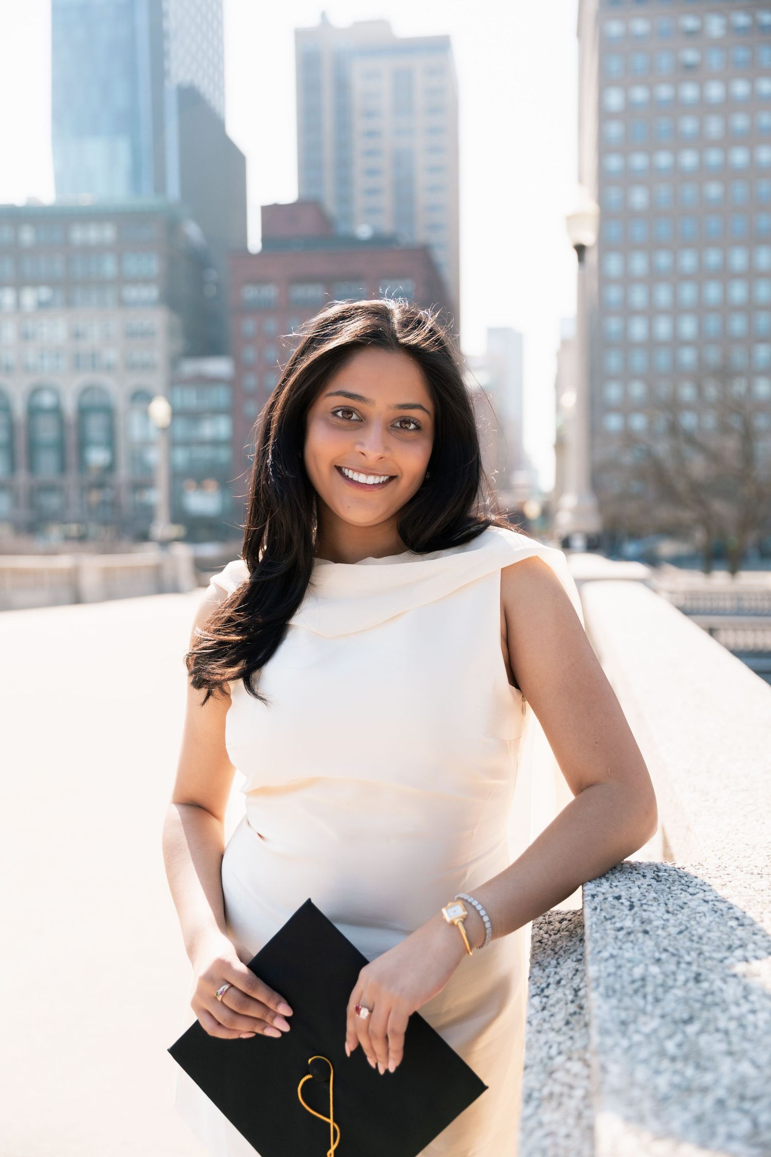 Graduate portrait session against a city skyline backdrop with modern buildings visible.