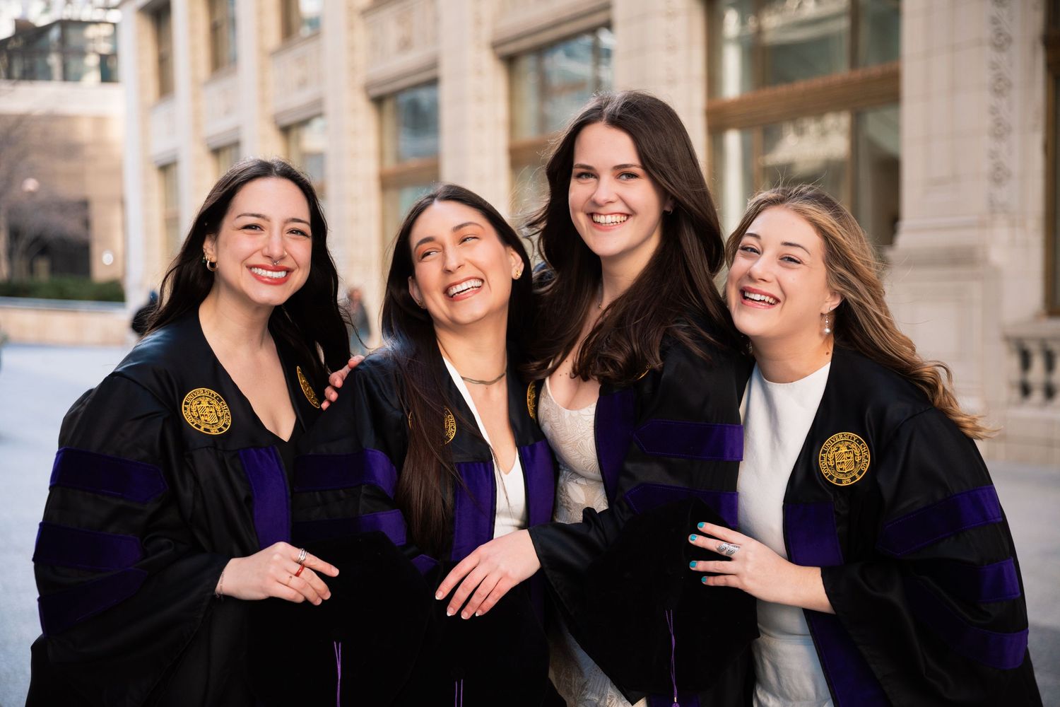 Group of graduates in black academic robes laughing together outdoors.