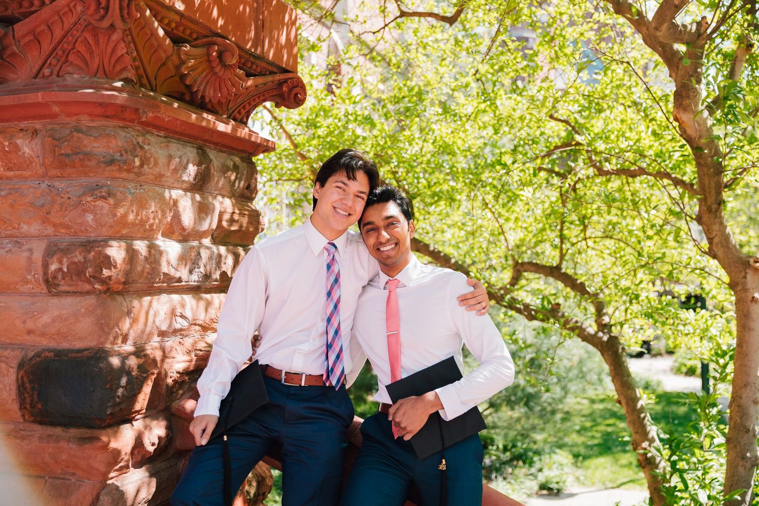 Graduation photo session with decorative brick architecture and green foliage in background.