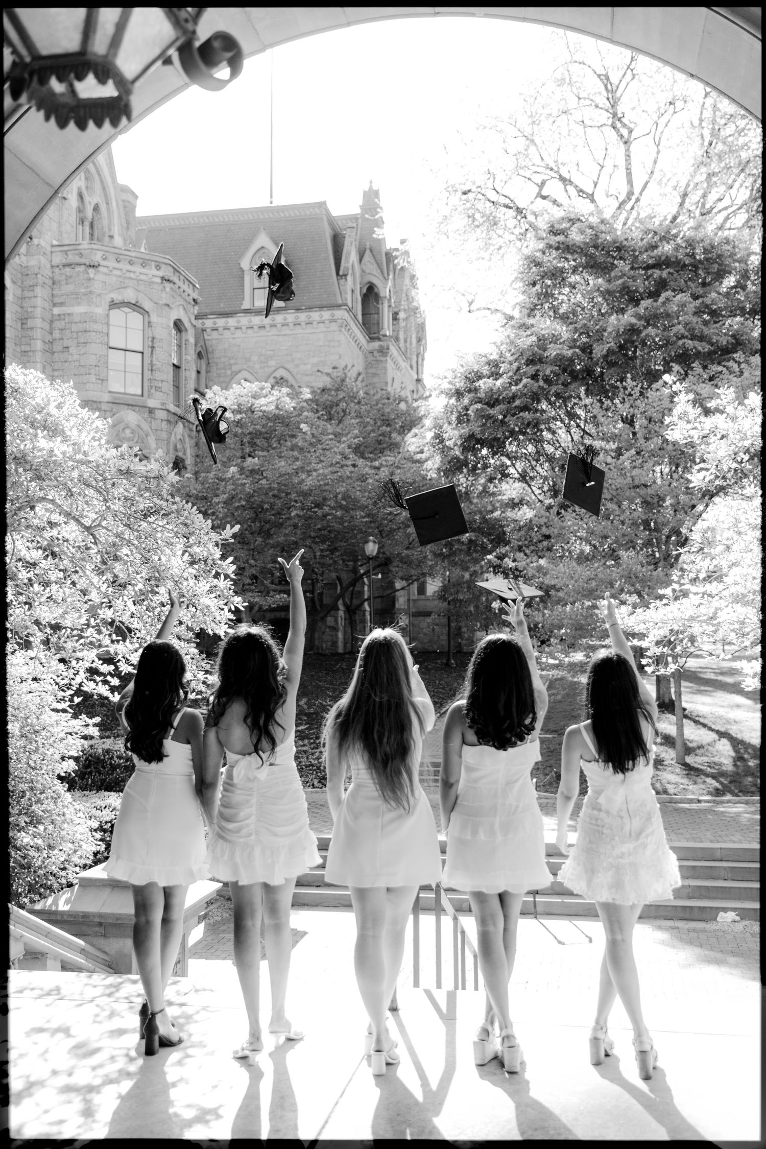 Graduates in matching white outfits smile and pose together outside a university building.