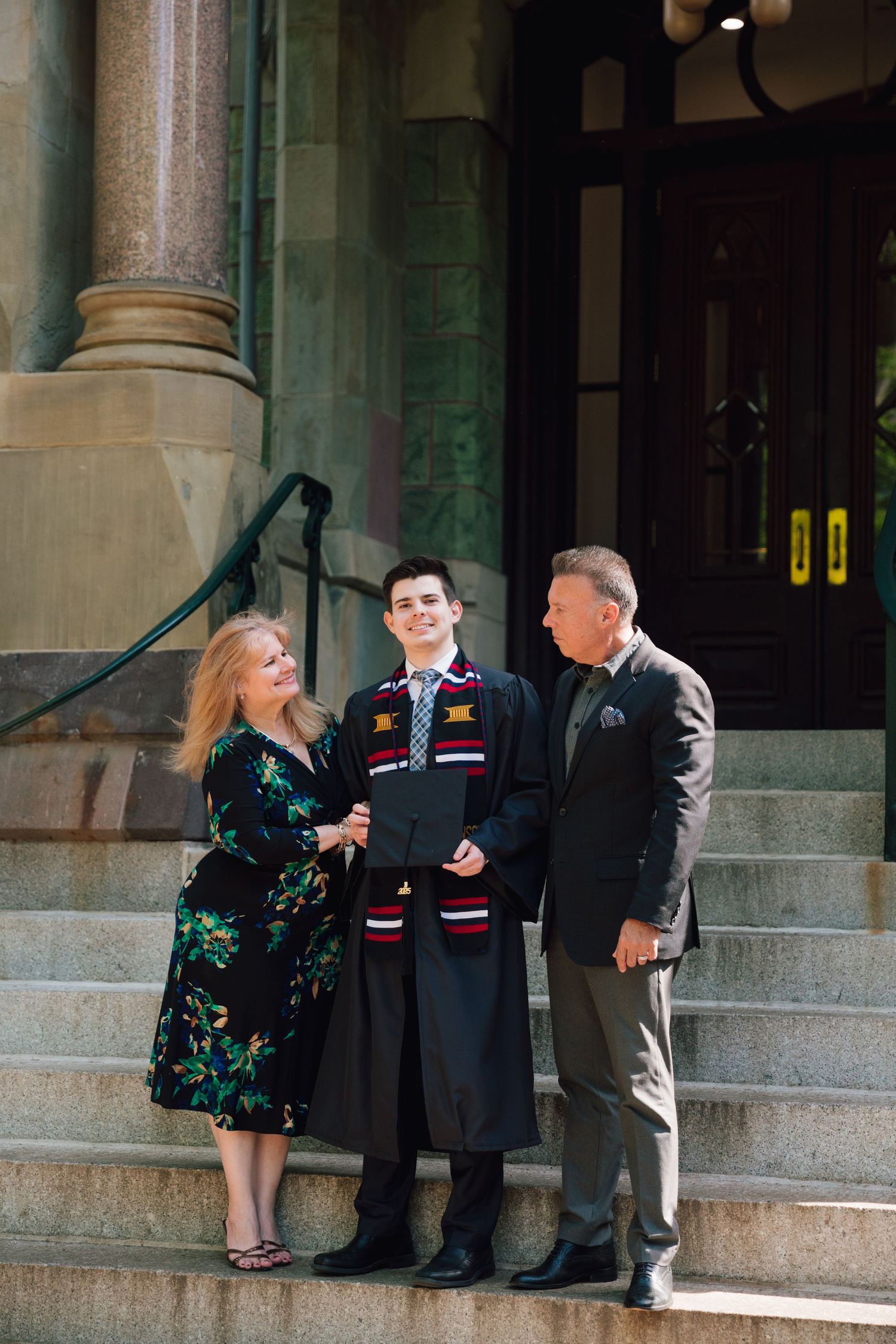 Family celebrating graduation on historic stone steps of university building.