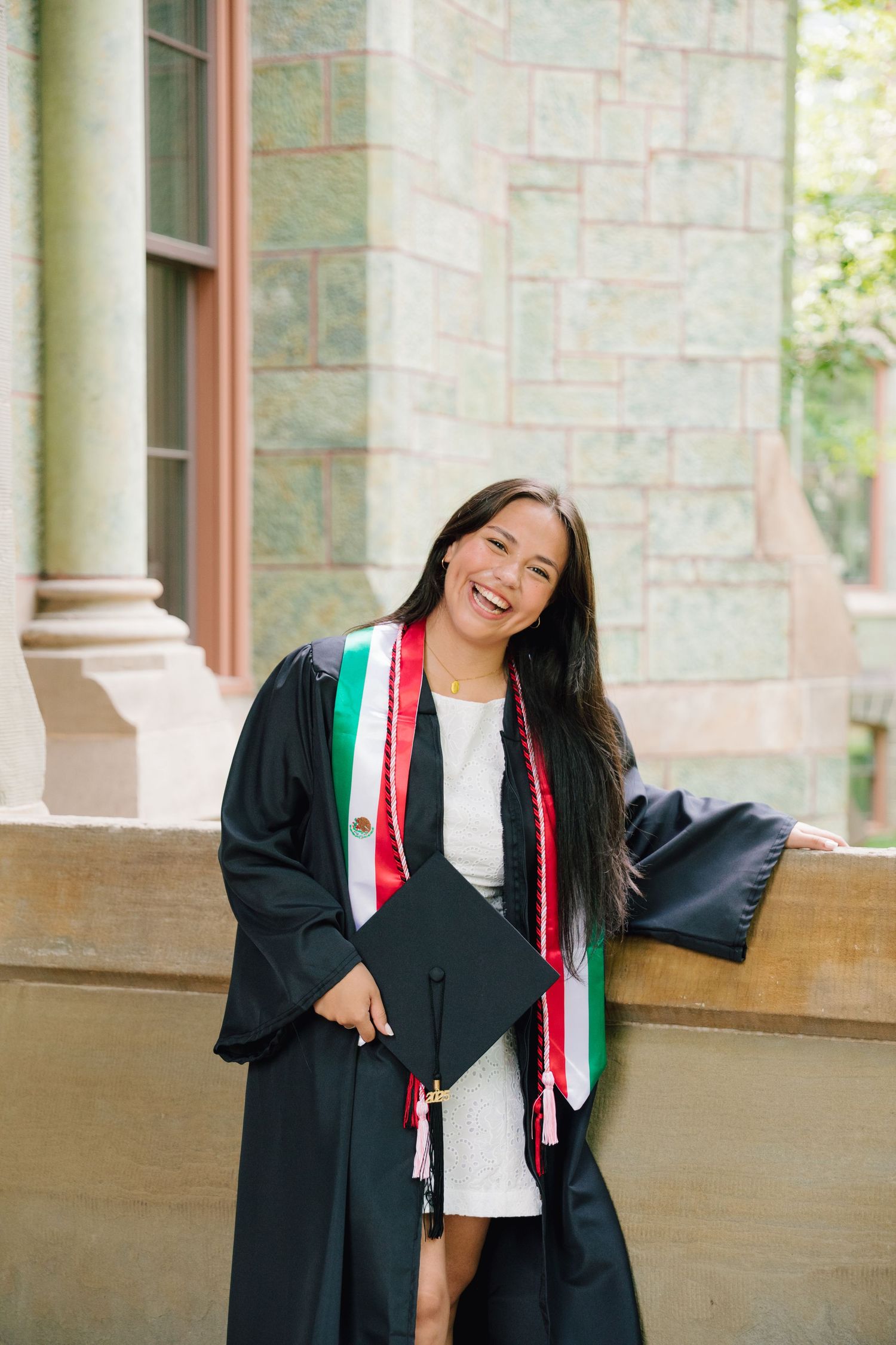 Graduate in academic regalia with colorful stole smiles while holding diploma cover.