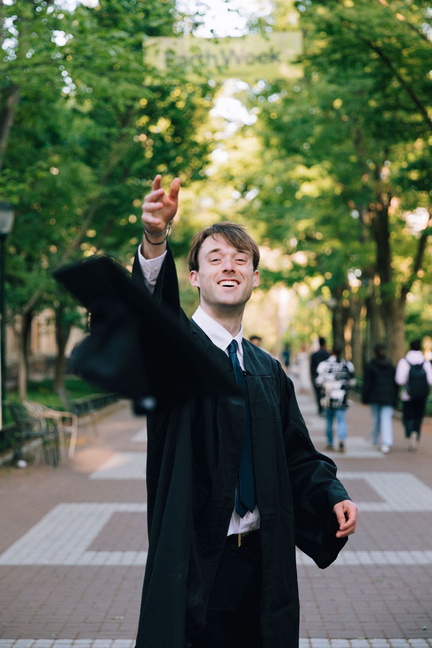 Celebratory poses in graduation attire on tree-lined campus pathway.