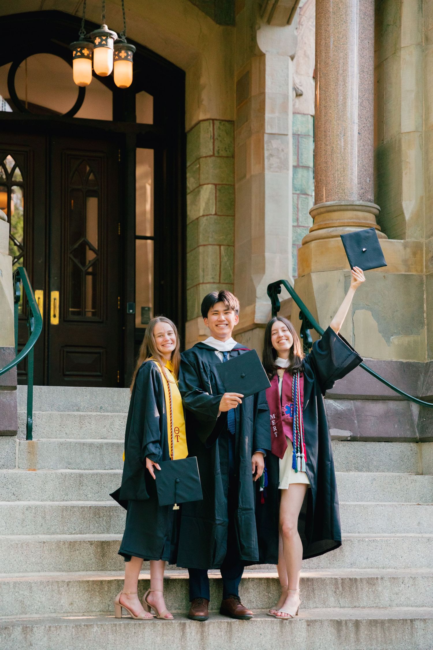 Students celebrate graduation on historic university steps wearing traditional academic regalia.