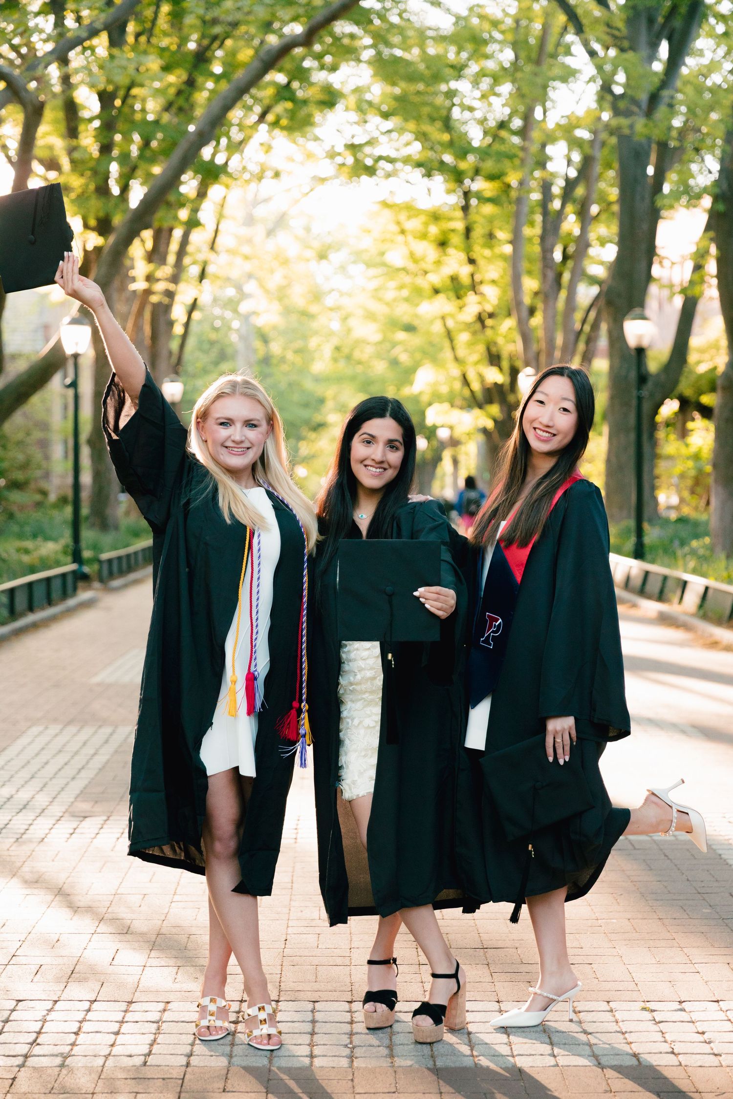 Group of graduates celebrating on brick pathway surrounded by trees.