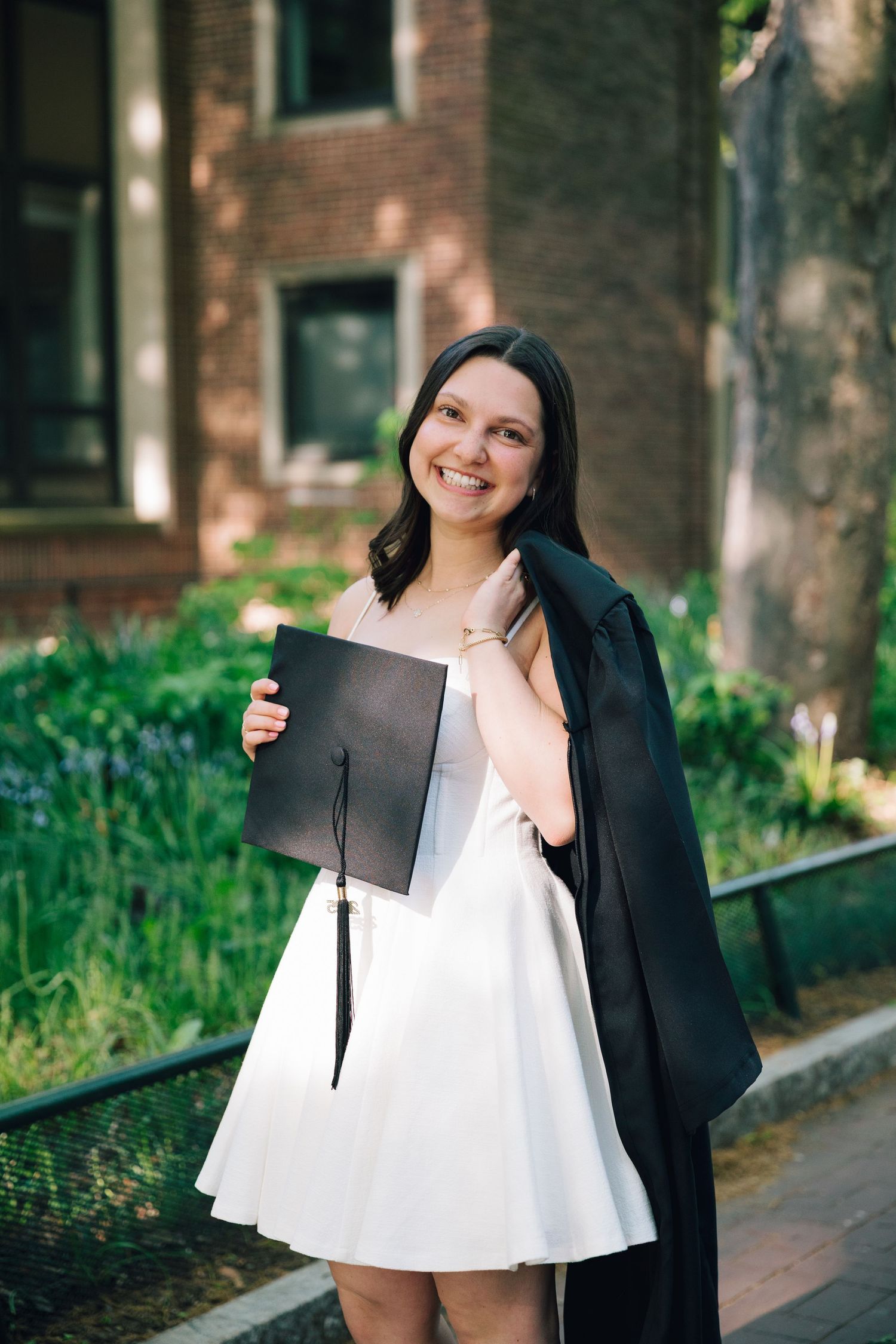 Graduate celebrates with diploma while wearing cap and gown outdoors.