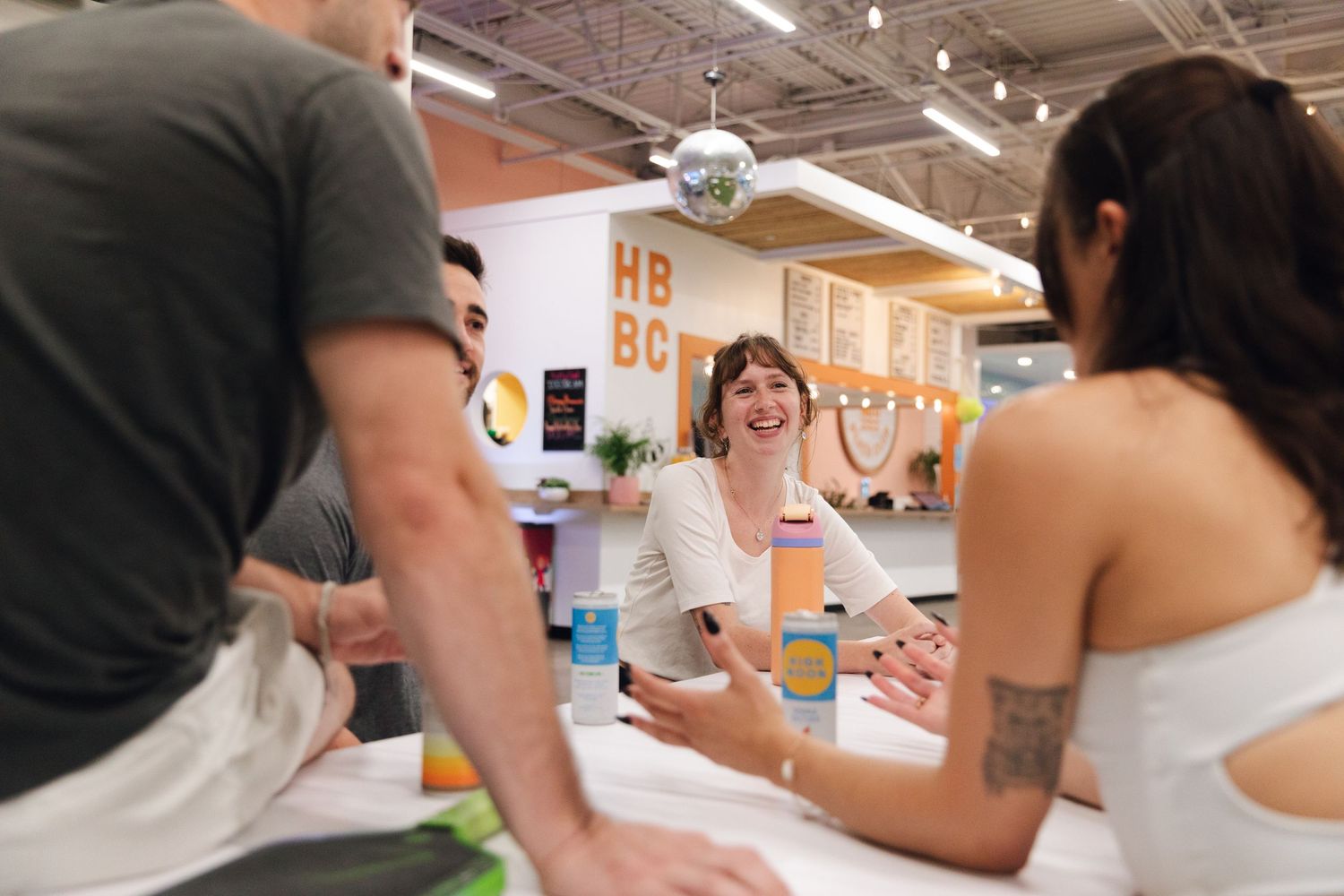 People laughing and socializing at a colorful cafe counter with a disco ball overhead.