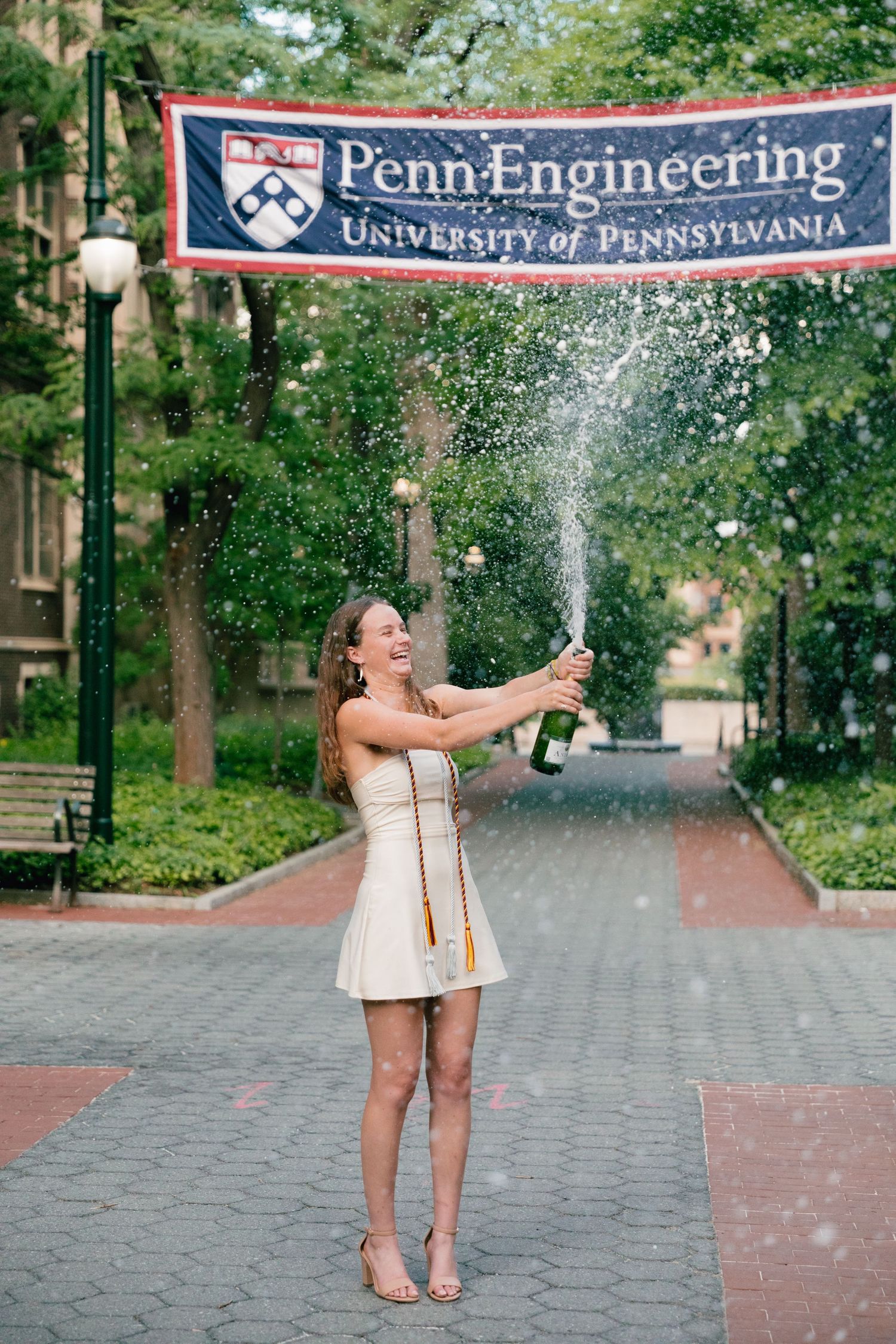 Graduates celebrate with champagne under University of Pennsylvania banners on campus.