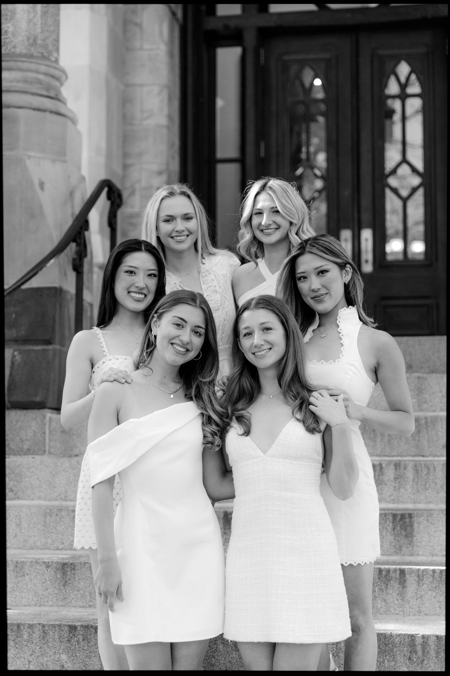 Black and white portrait of graduates in white dresses gathered on ornate stone steps.