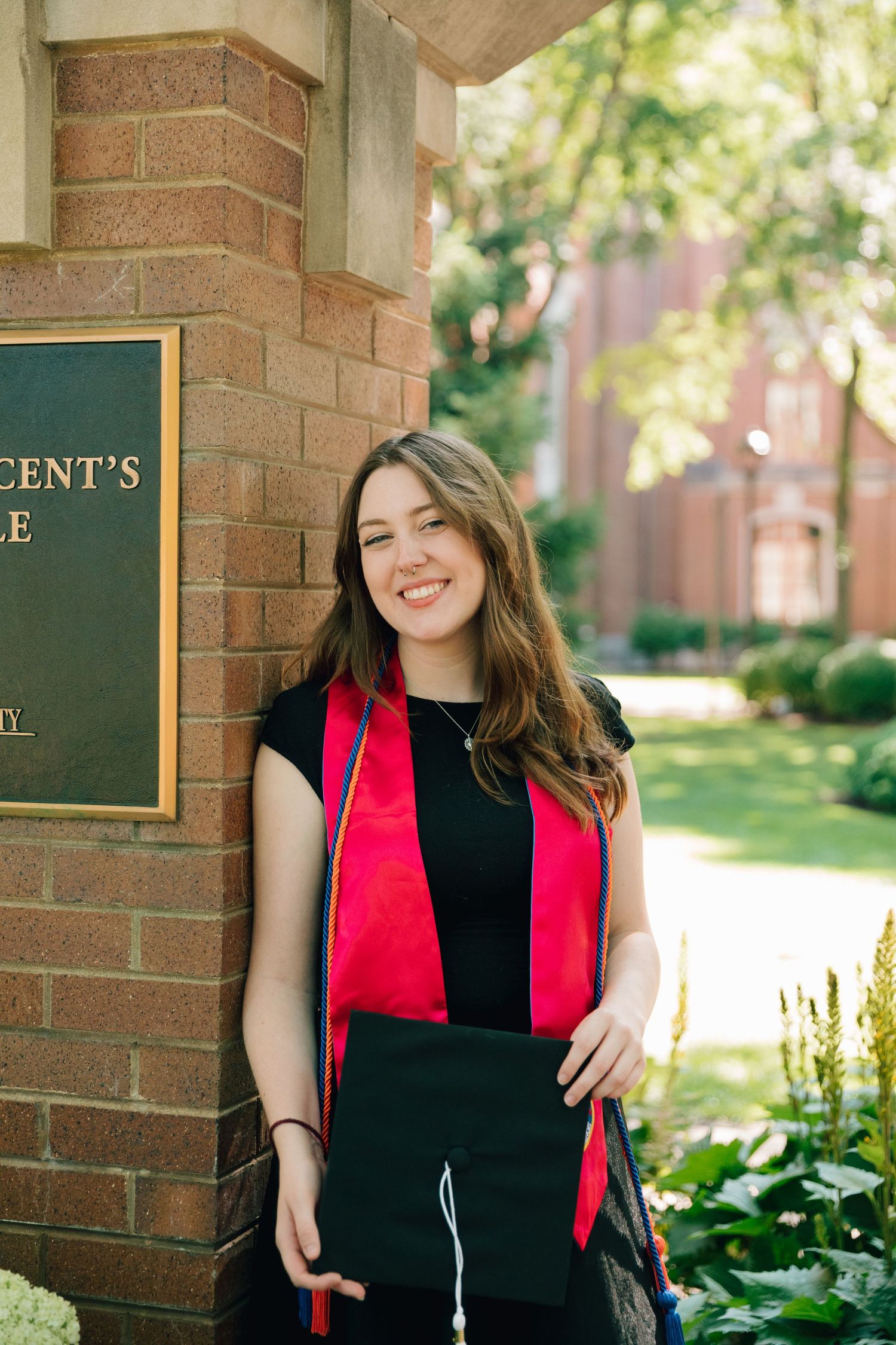 Graduate posing by Saint Vincent's Circle brick sign wearing red and black graduation attire.