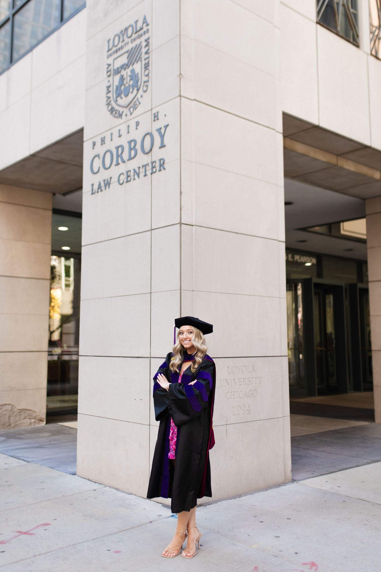 Graduate poses outside Corboy Law Center wearing doctoral regalia.