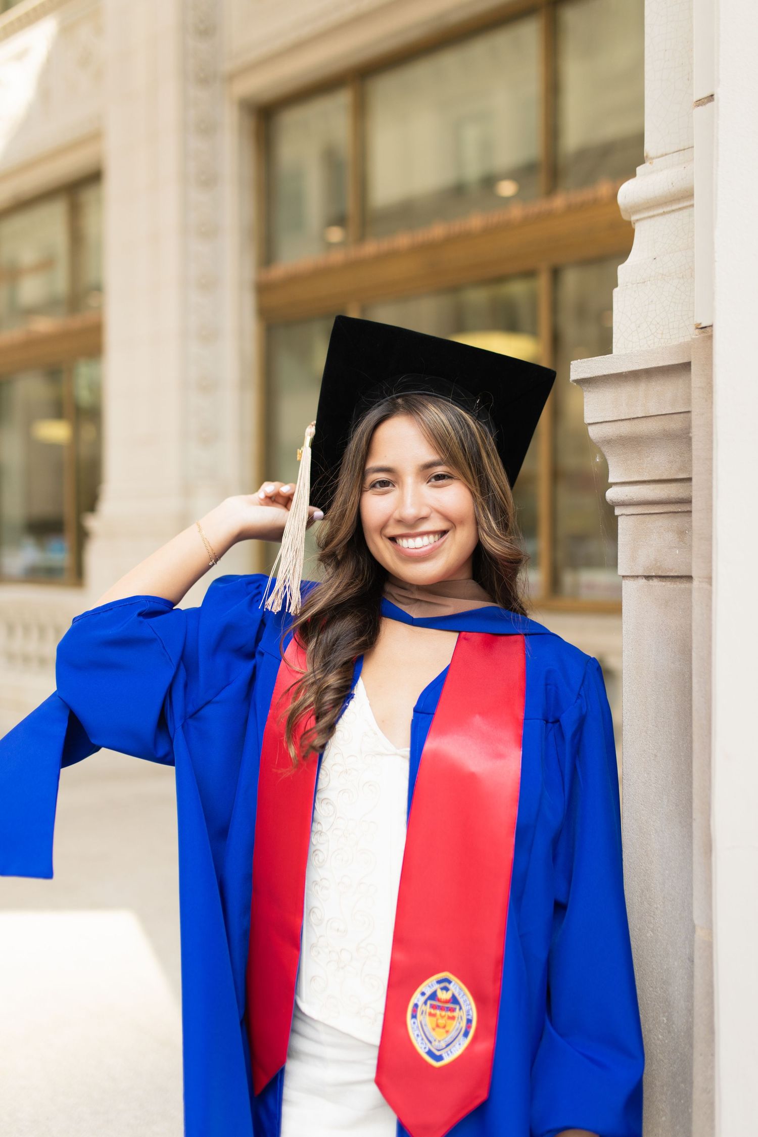 Graduate in blue and red academic regalia poses by university columns.