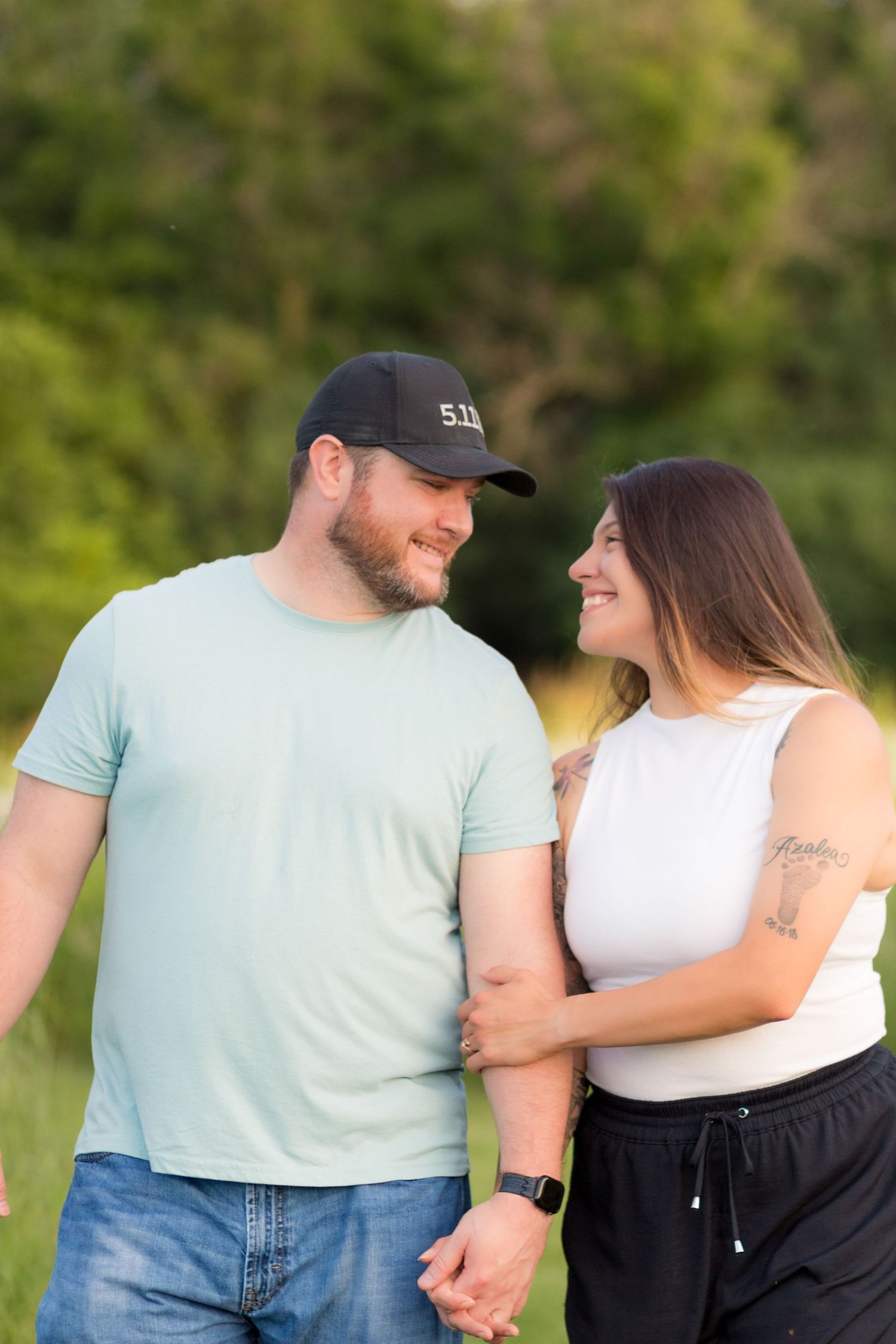 A couple in matching blue and white outfits laugh and embrace while standing outdoors in a green setting.