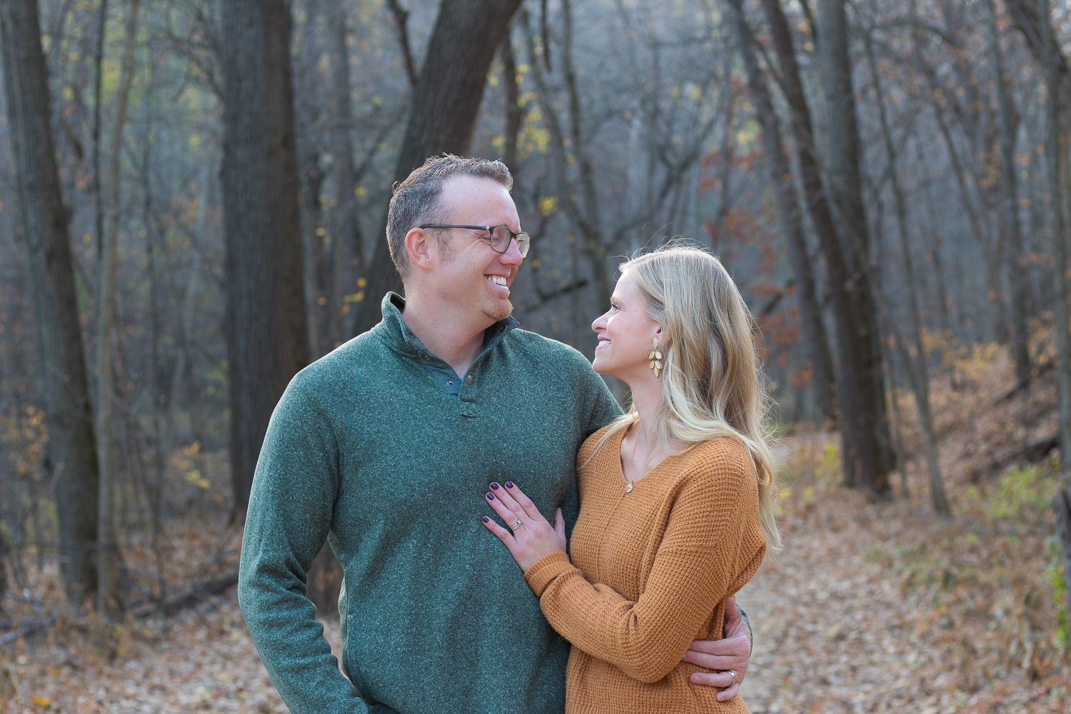 A couple shares a loving moment while standing in autumn woods.