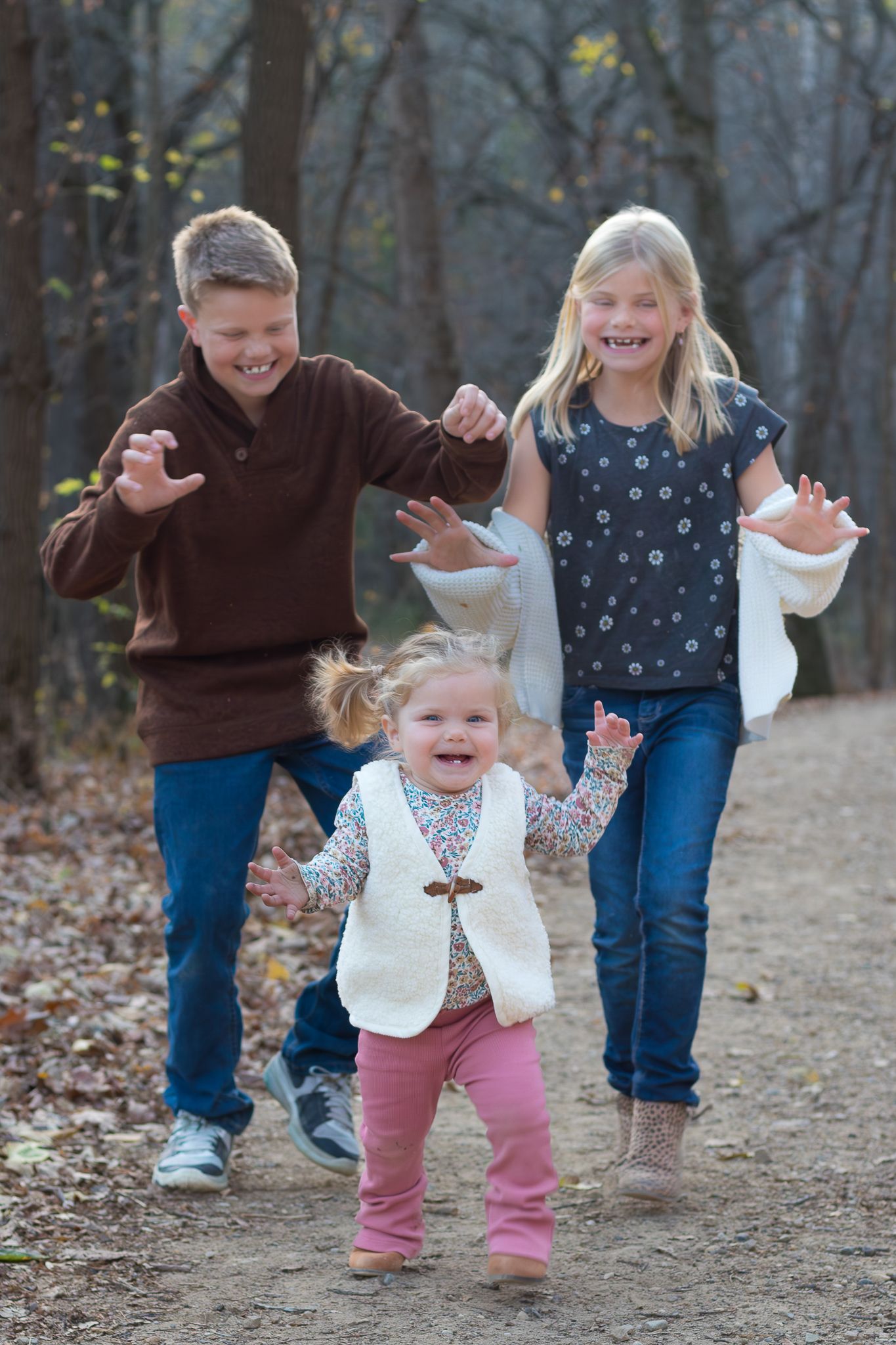 Three playful figures dance and laugh together on a woodland trail.
