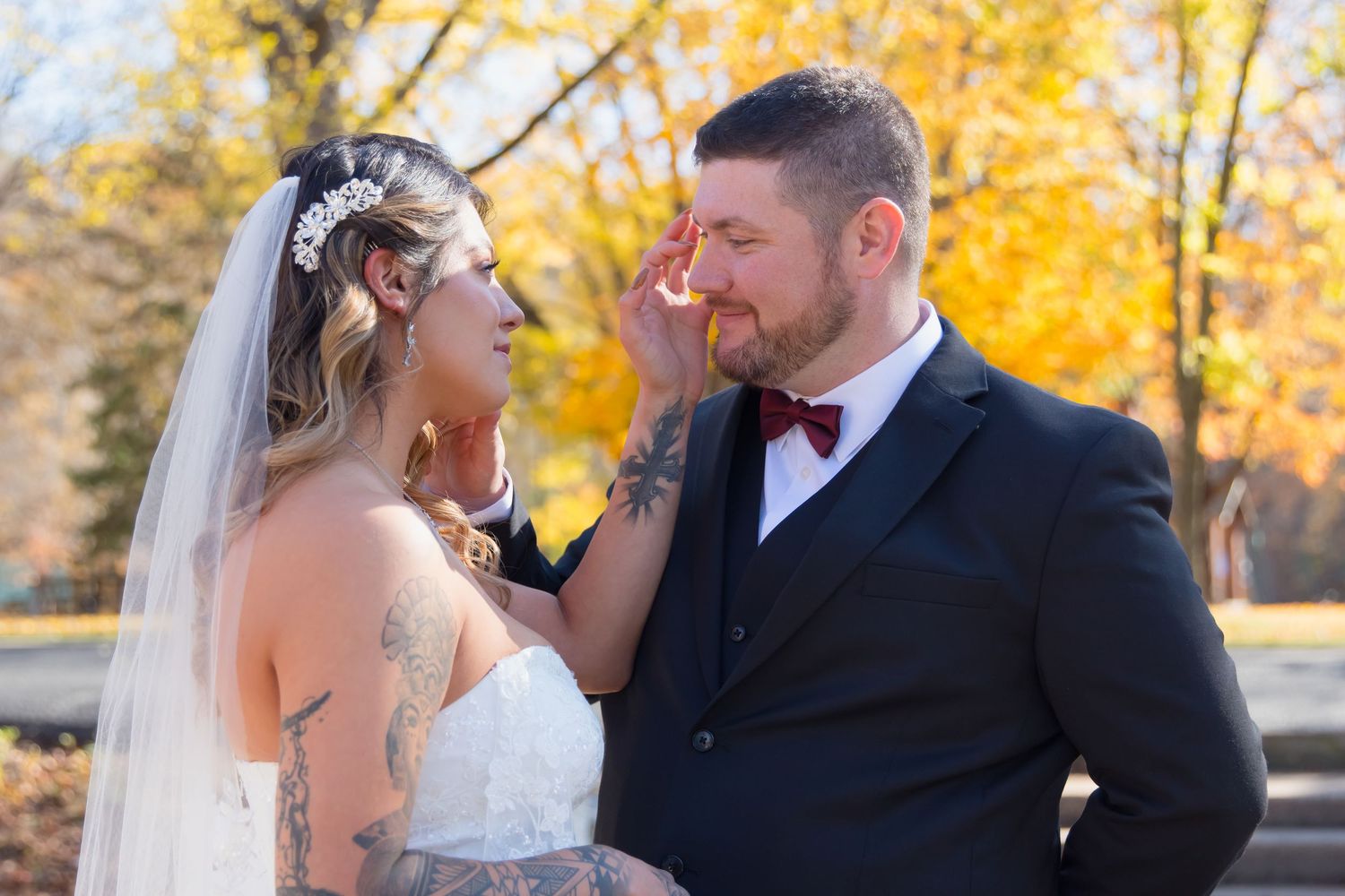 Newlywed couple shares romantic moments outdoors during autumn with golden foliage in the background.