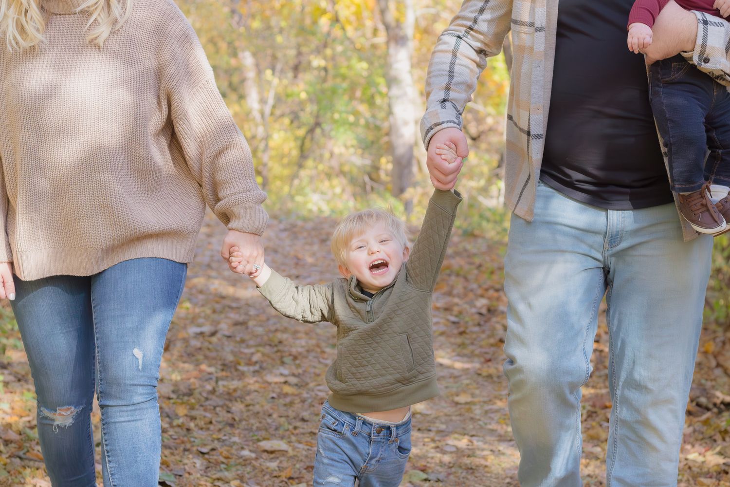 Child joyfully jumping while holding hands with parents on an autumn trail.