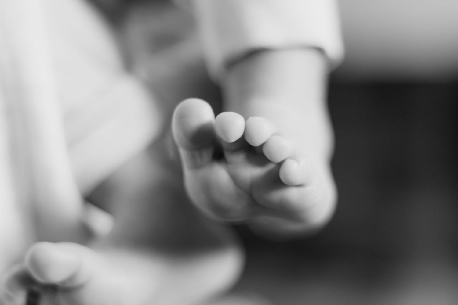 Close-up black and white photo of a tiny baby foot showing delicate toes against a soft blurred background.
