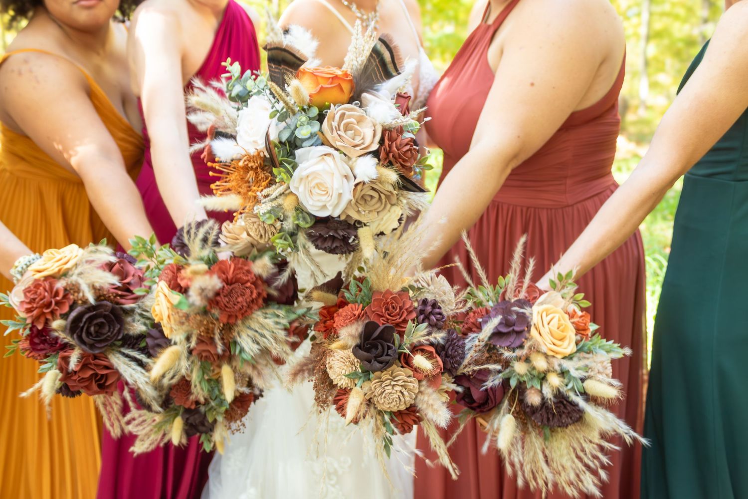 Bridesmaids holding stunning fall-themed bouquets with burgundy and cream flowers against an outdoor backdrop.
