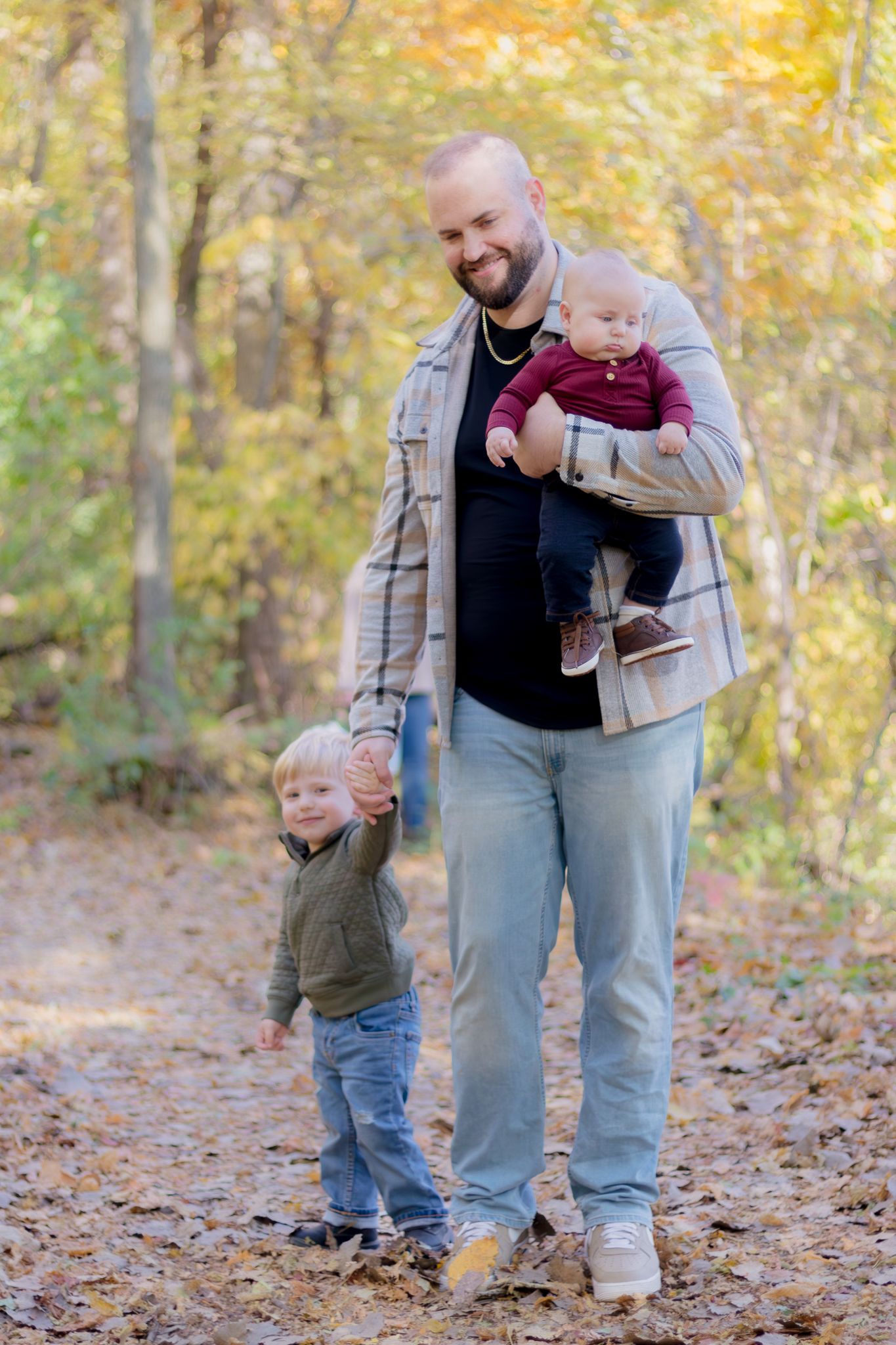 Parent and children walking along a fall forest path covered in golden leaves.