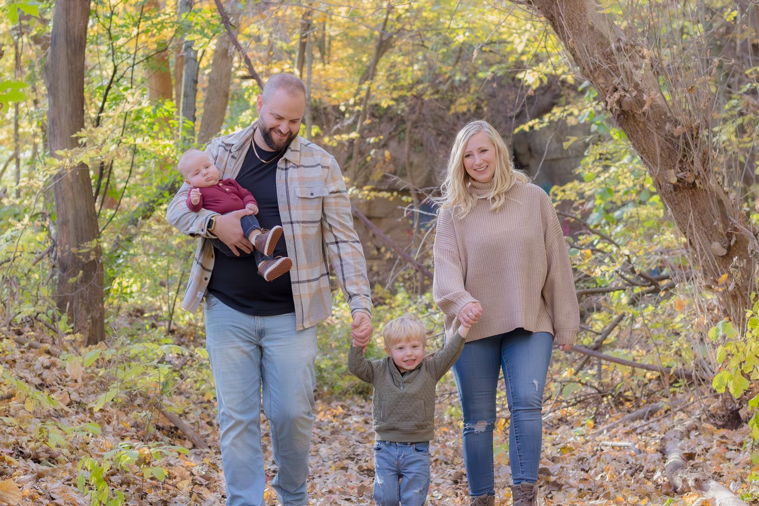 Family walking together on a leaf-covered autumn trail through golden woods.