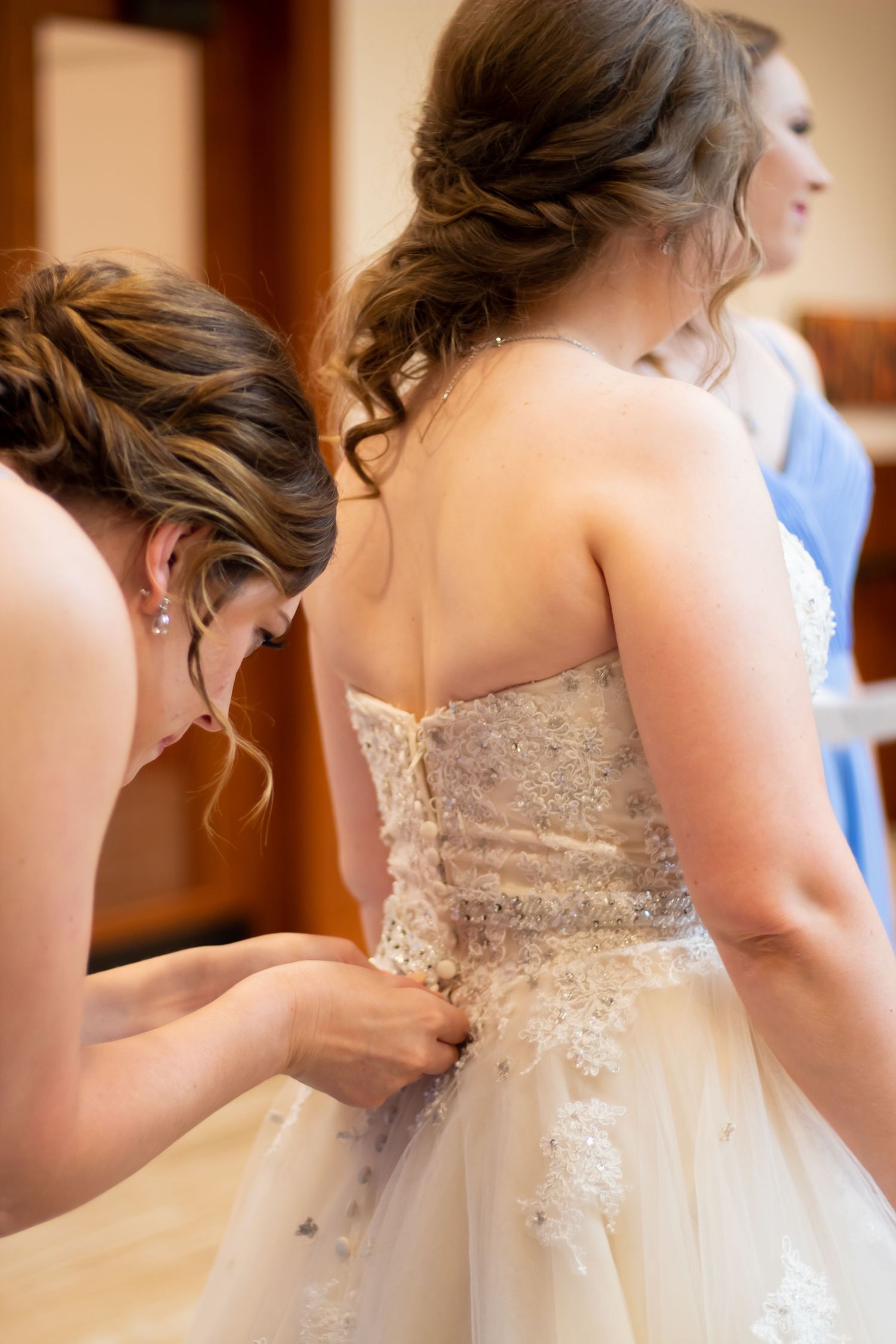 A close up of someone helping to fasten a delicate white lace wedding dress with intricate detail.