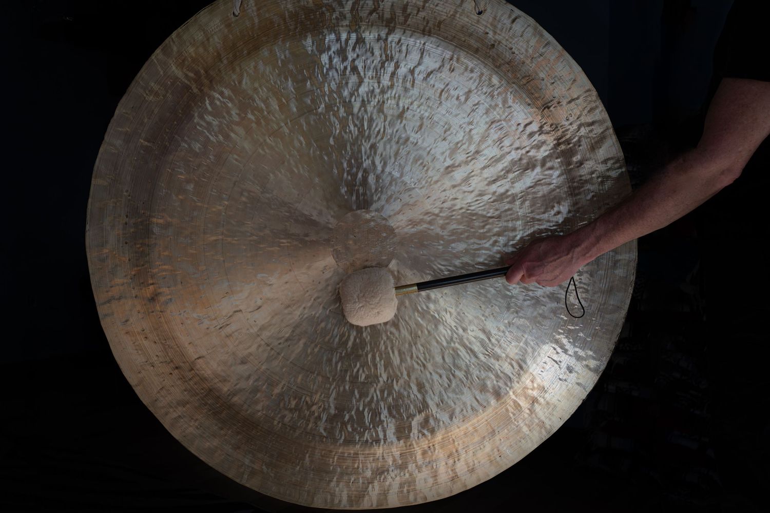 Close-up of hand striking large meditation gong with textured metallic surface.