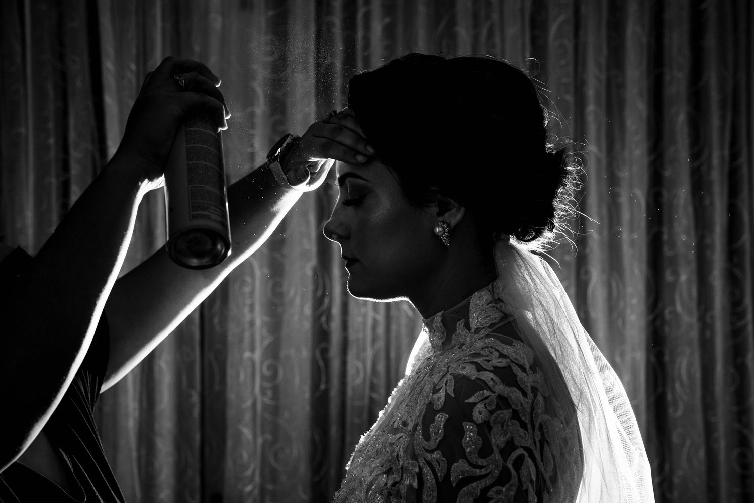 Silhouette of bride getting ready in dramatic black and white lighting against curtained backdrop.