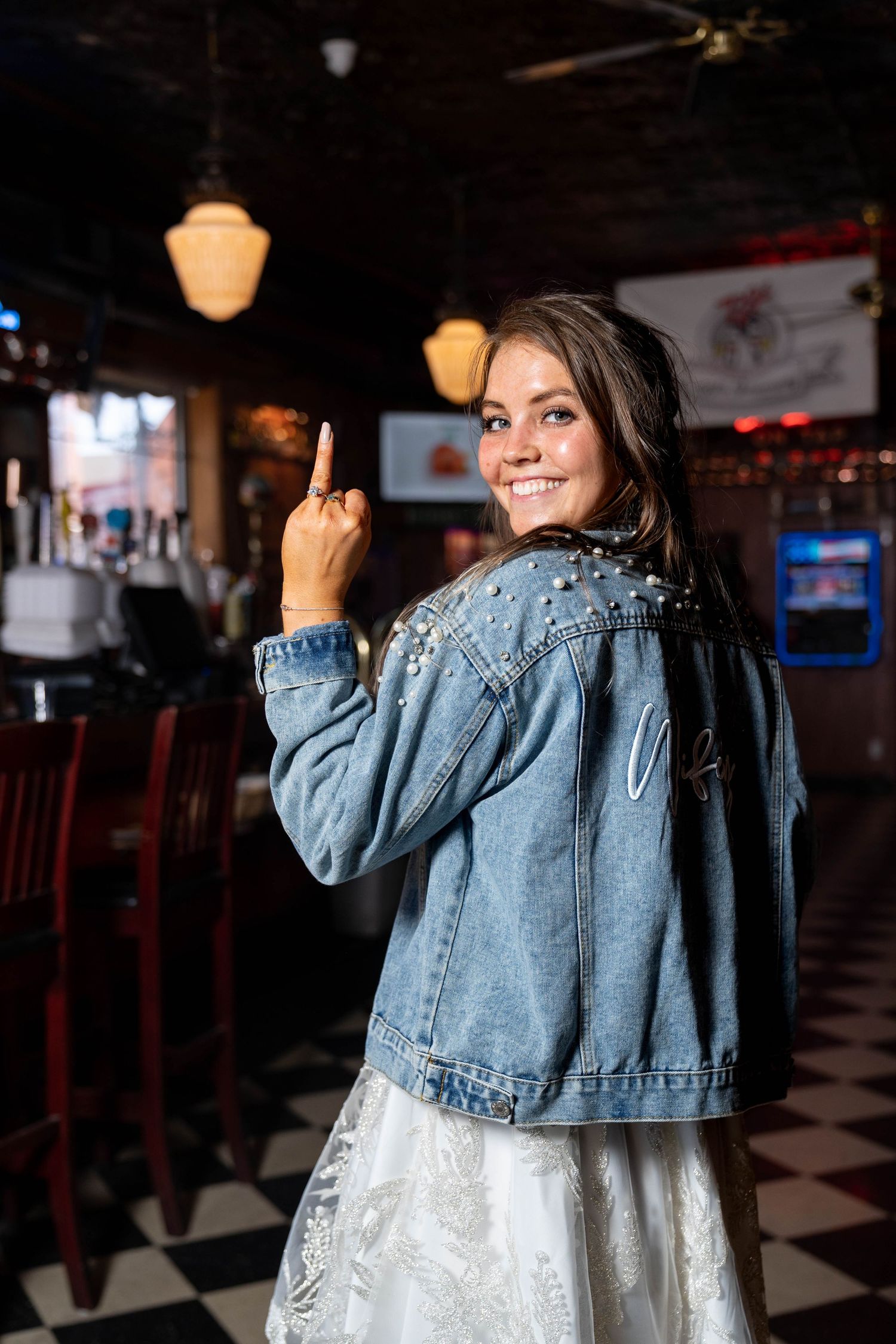 Woman in denim jacket and white dress making playful gesture in retro diner.