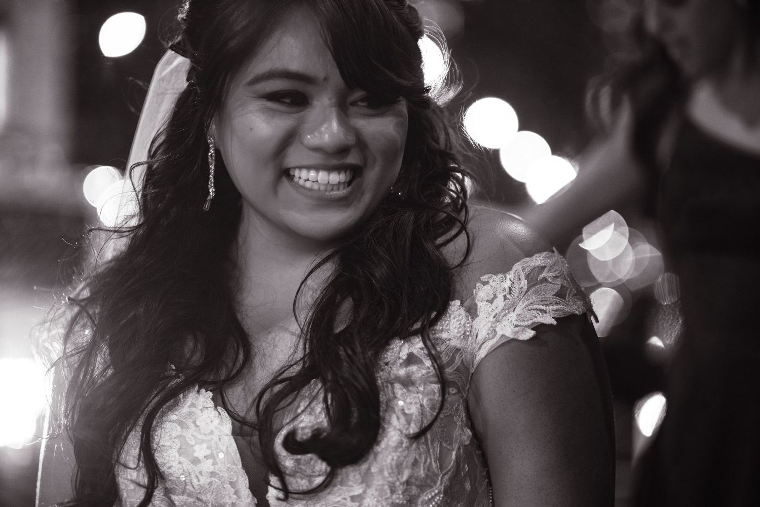Black and white portrait of radiant bride smiling with bokeh lights in background.