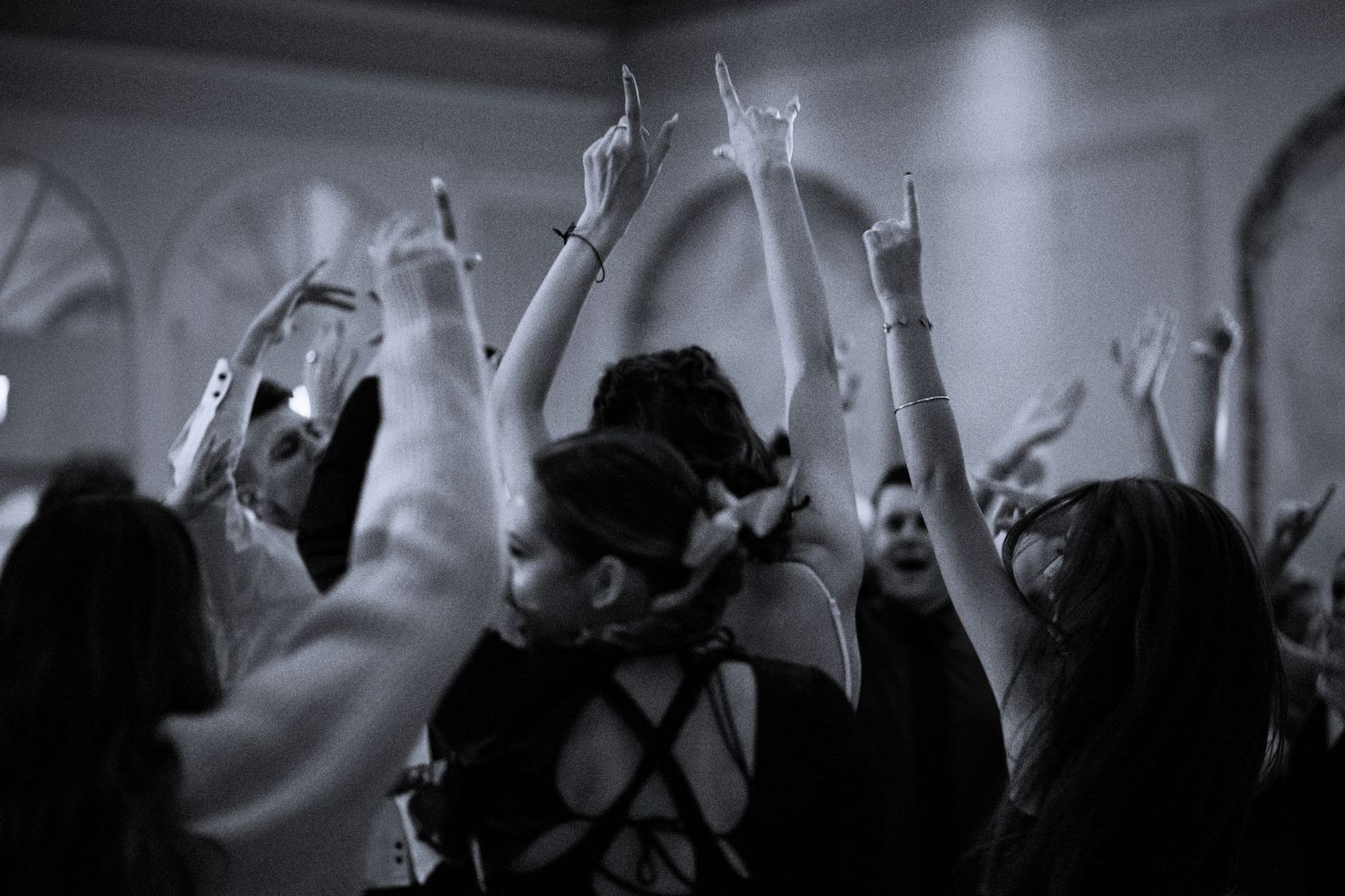 Black and white photo of wedding guests dancing with hands raised in celebration.