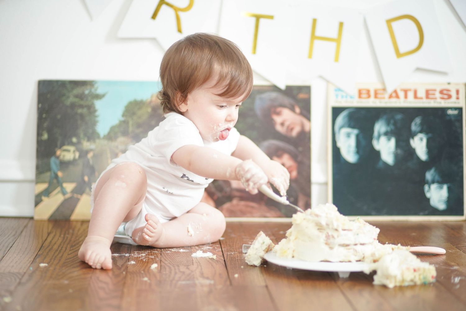 Baby playing with smashed cake near Beatles albums under birthday banner.