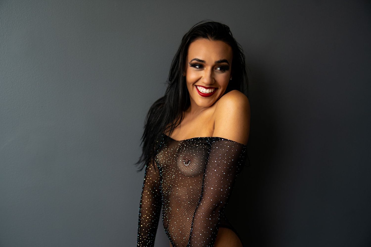 Portrait of someone in sparkly sheer dress against grey backdrop.