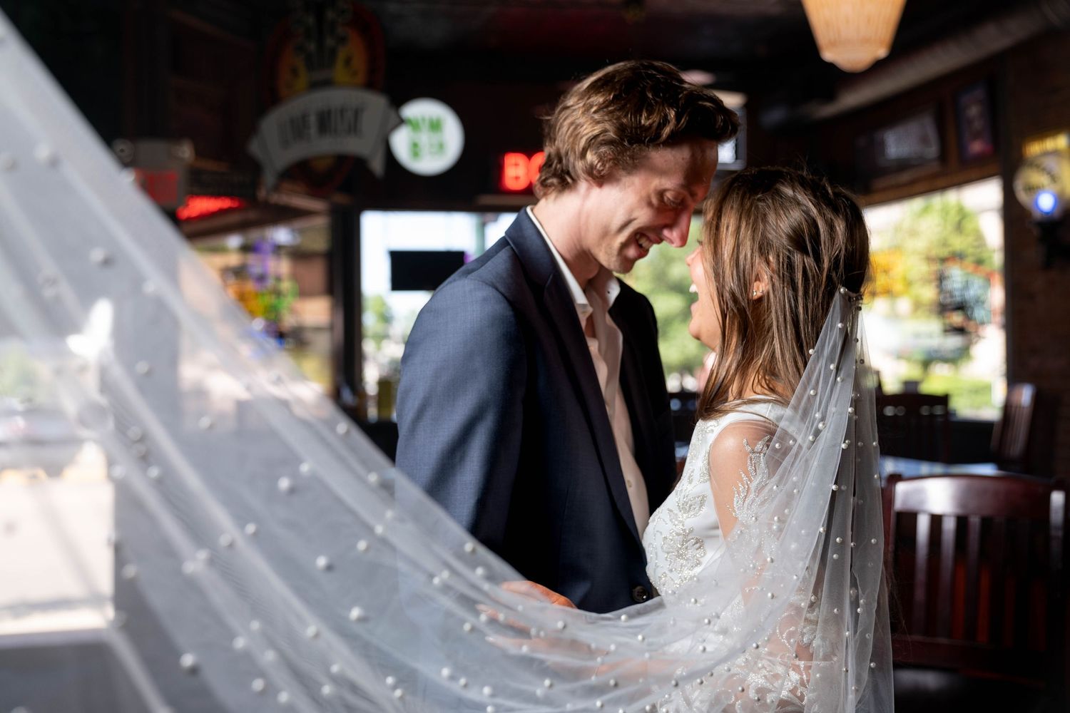 Intimate moment between couple in dim bar setting with decorative veil.