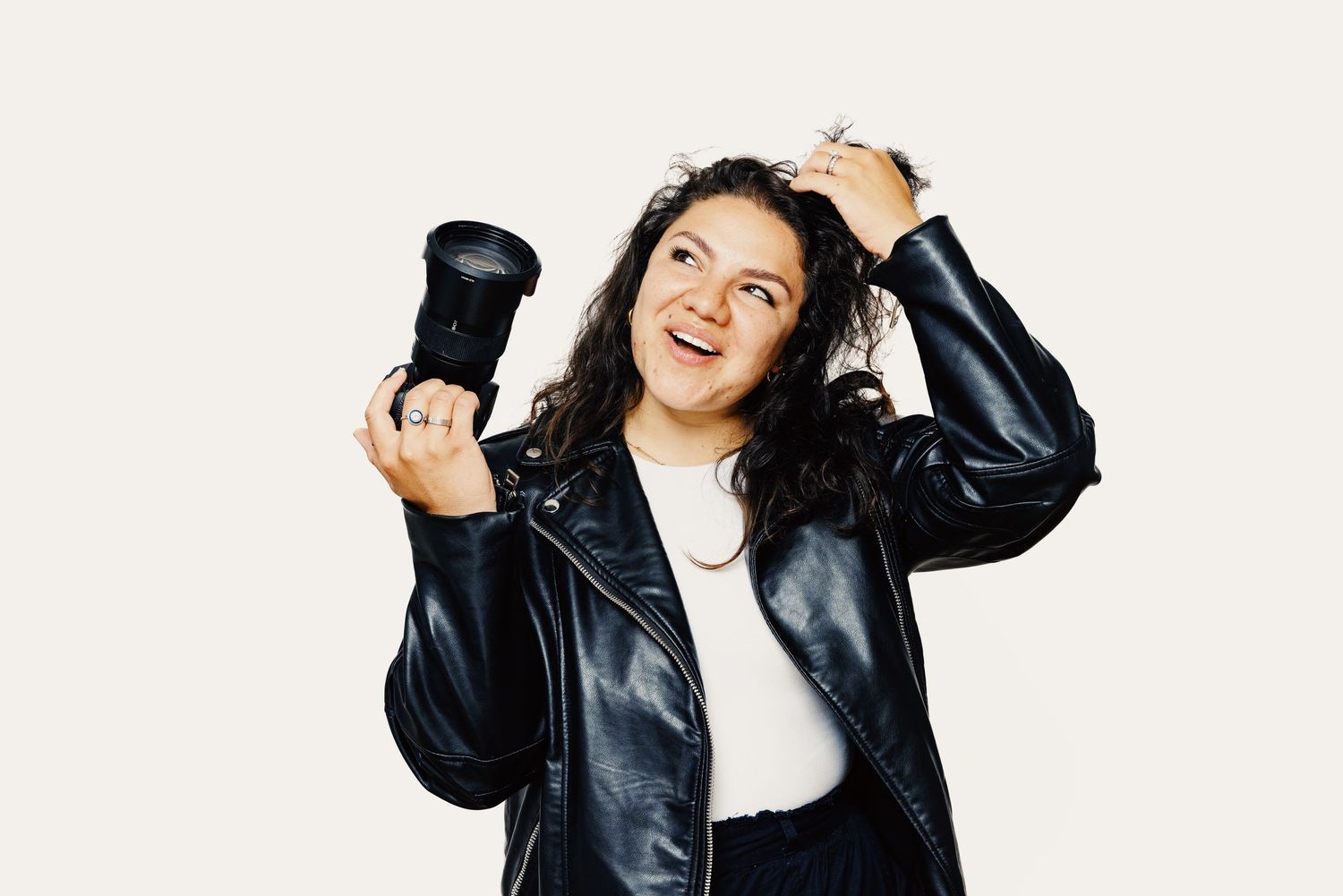Photographer in leather jacket holding camera with joyful expression against white background.