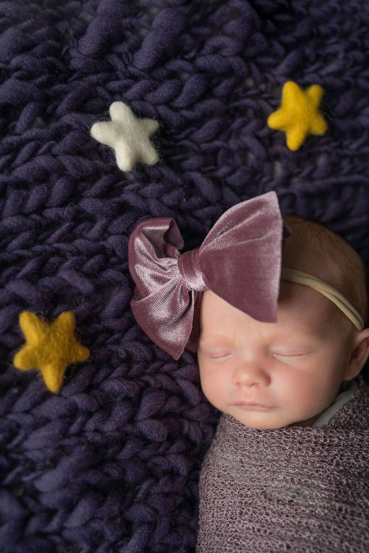 Sleeping newborn on navy knit blanket with pink bow and yellow star decorations.