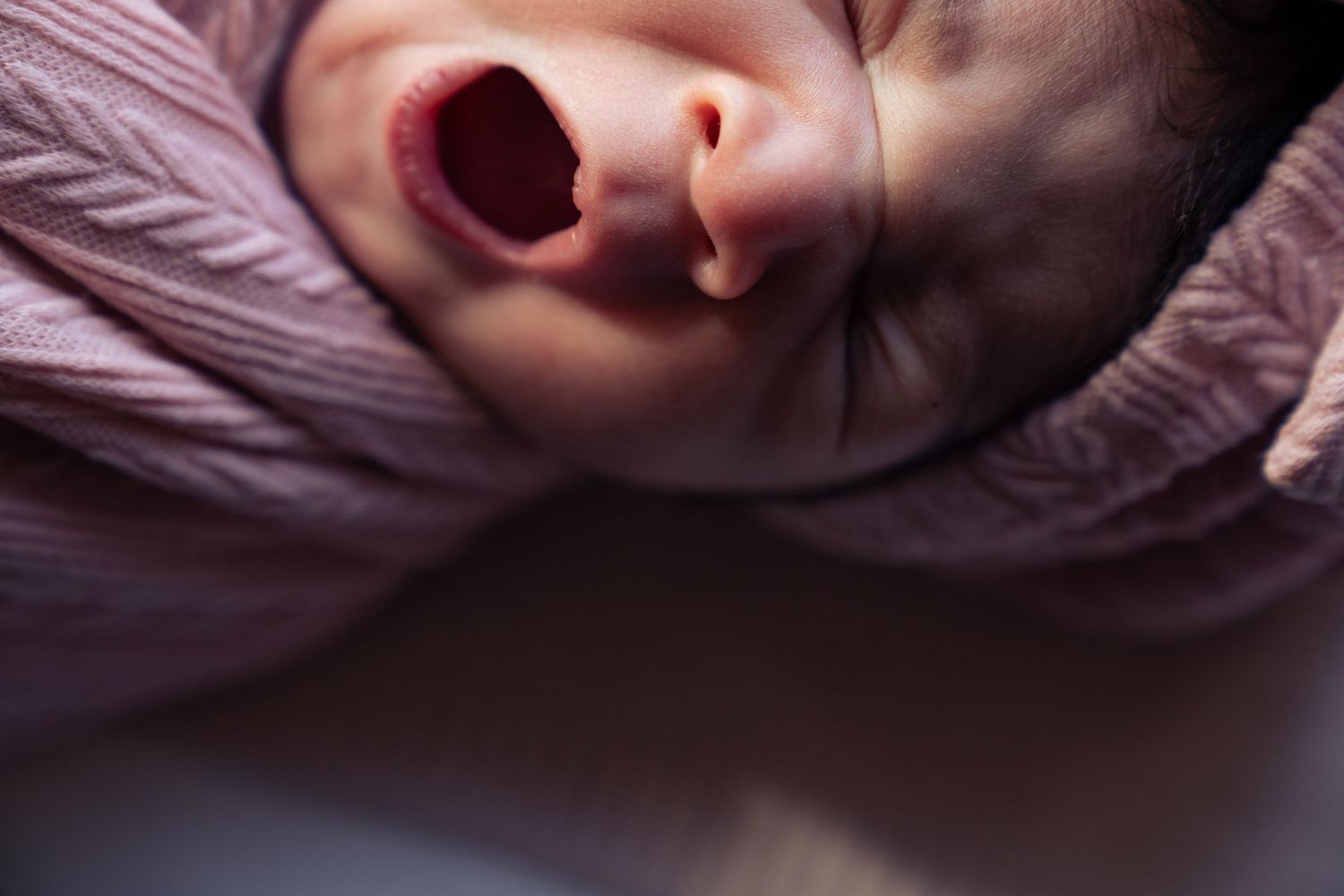 Close-up of yawning baby's face against purple bedding.