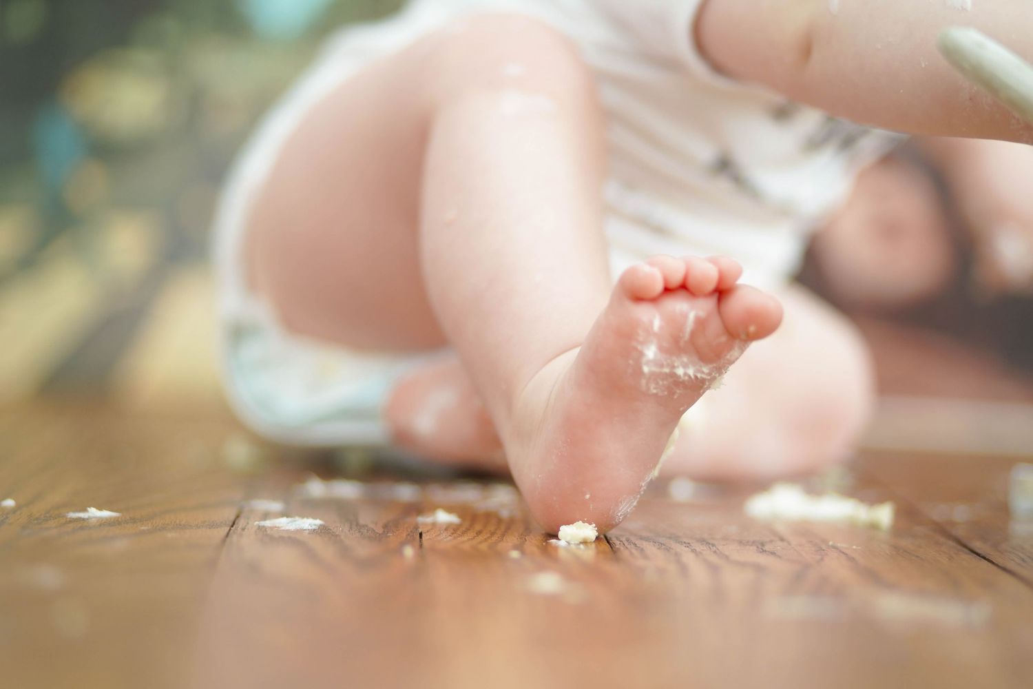 Tiny baby foot rests on a wooden floor in soft natural lighting.