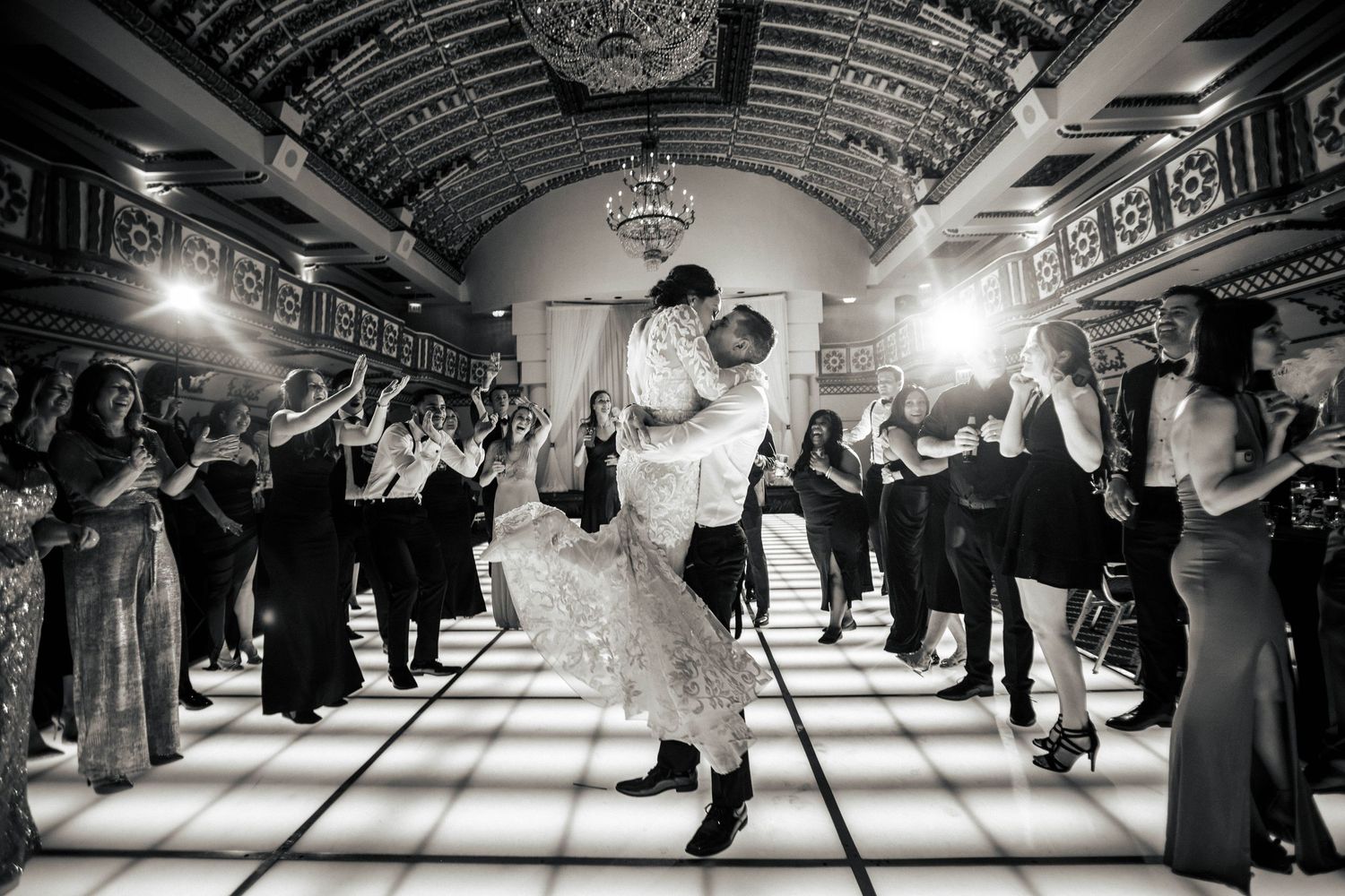 Black and white photo of couple's first dance surrounded by guests in an elegant ballroom.