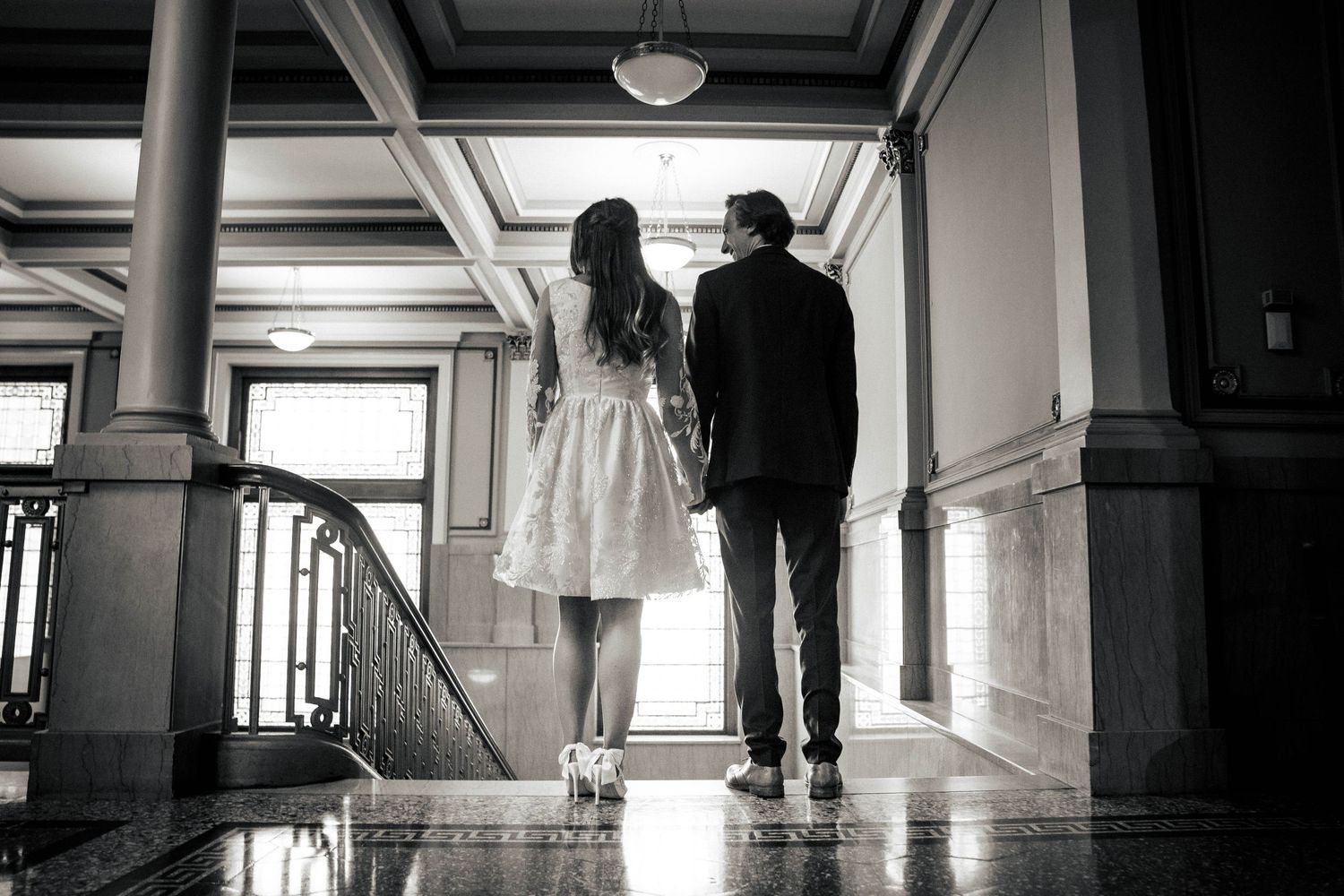 Black and white photo of couple walking down elegant hallway.
