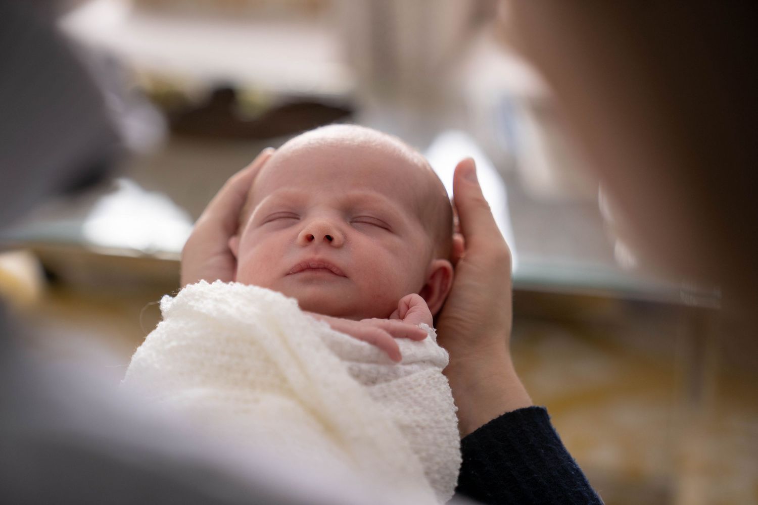 Newborn baby swaddled in white blanket being cradled.