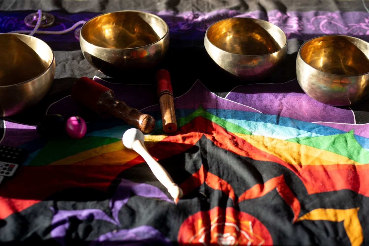 Tibetan singing bowls arranged beside rainbow flags and ritual items on a purple fabric backdrop.
