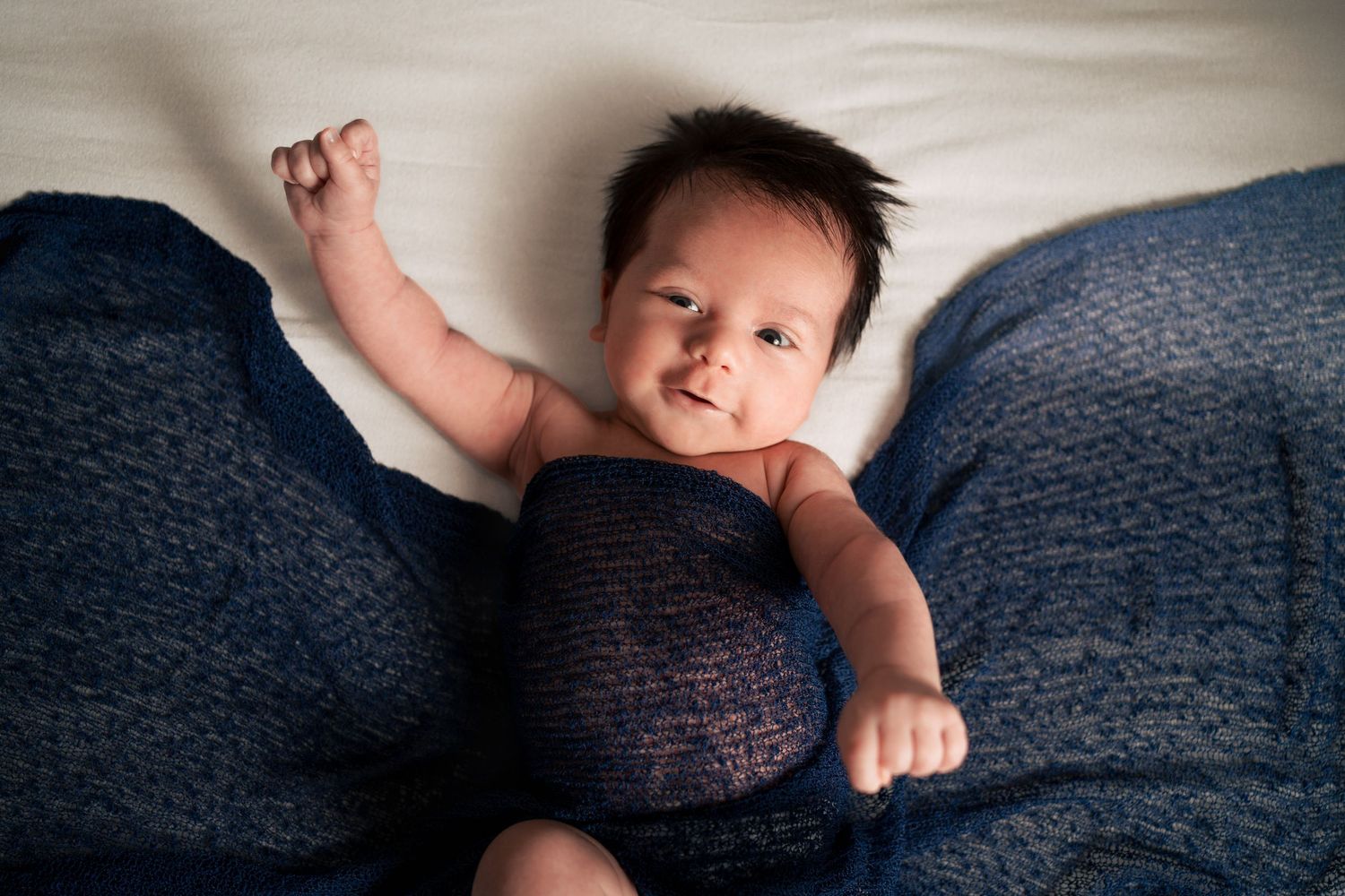 Baby wearing navy onesie lies on dark blue textured blanket.