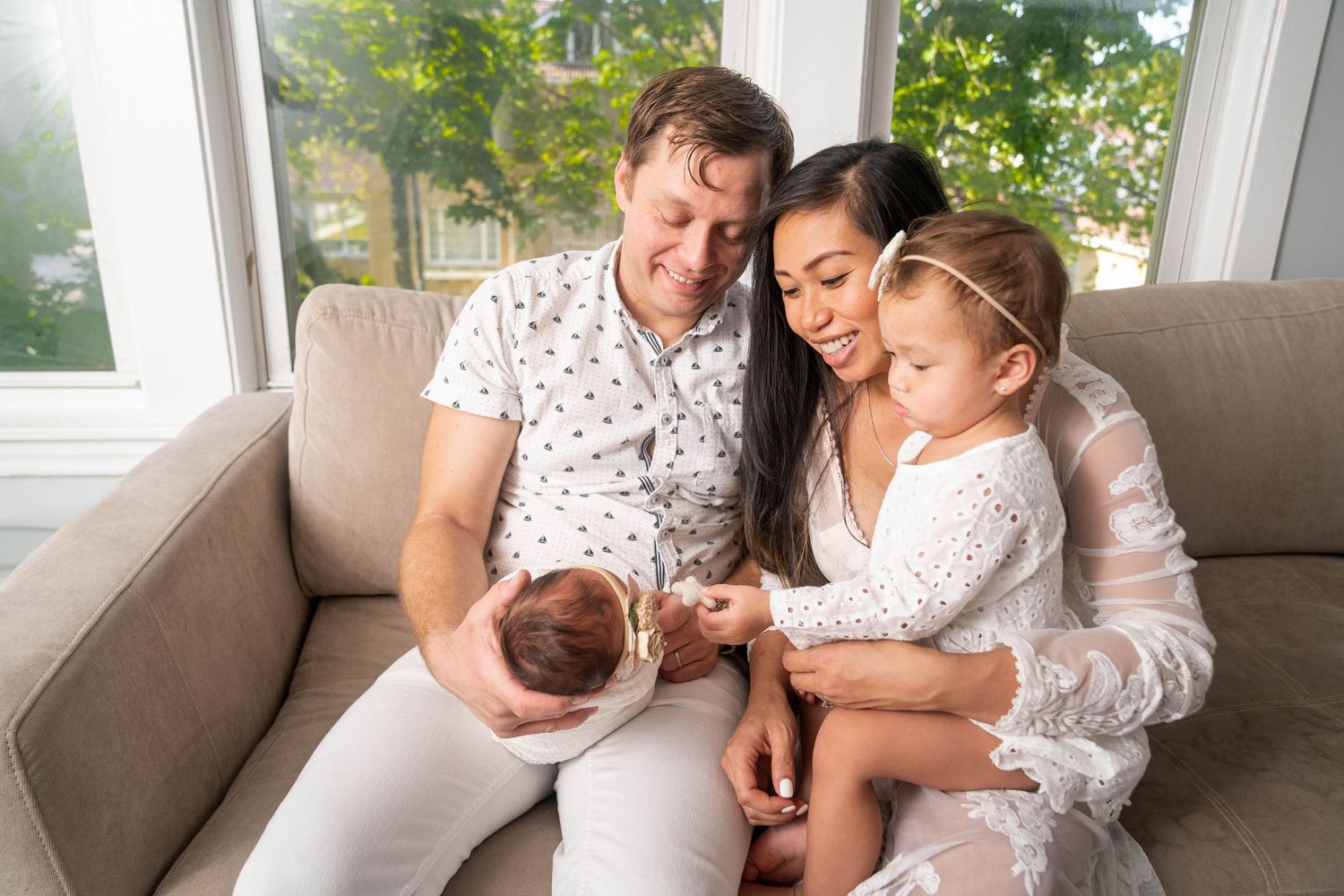 Family in white attire cuddling together on couch with newborn.