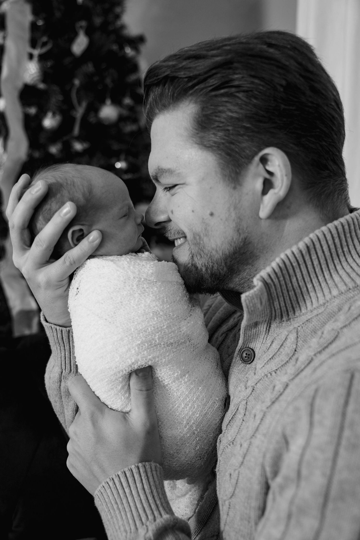 Tender moment between parent and newborn wrapped in white blanket.