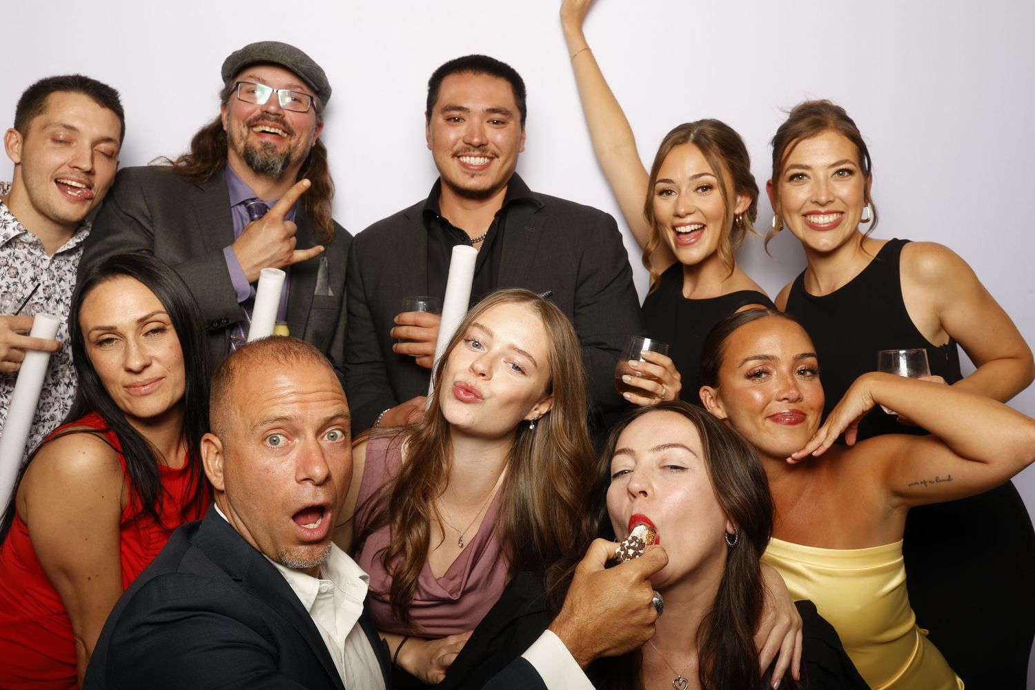 Group of friends making silly faces and poses together at a party photo booth against white background.